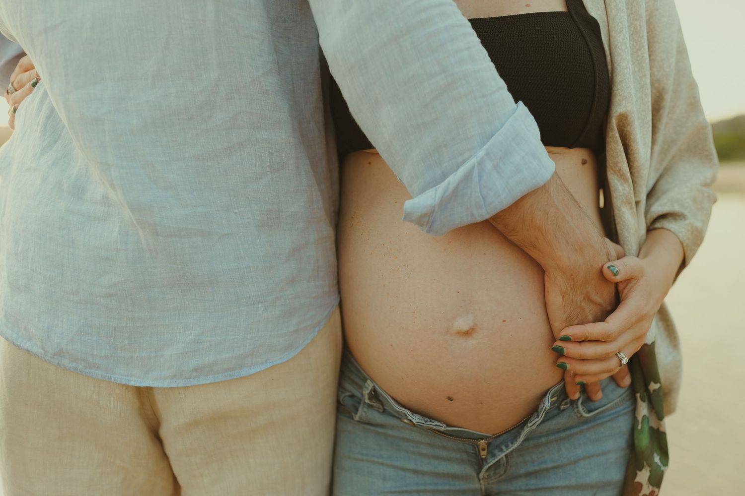 Intimate maternity photo session showing pregnant belly on a sandy beach at sunset.
