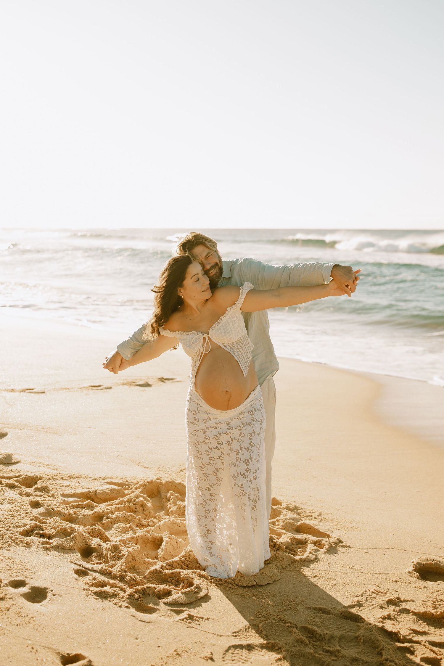 Carefree couple dancing together on a sunny beach with ocean waves in the background.