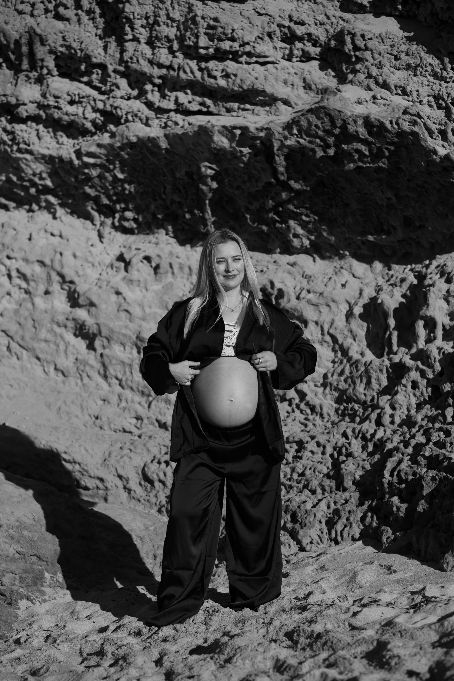 A person in black clothing stands smiling against a rocky cliff wall in a black and white photo.