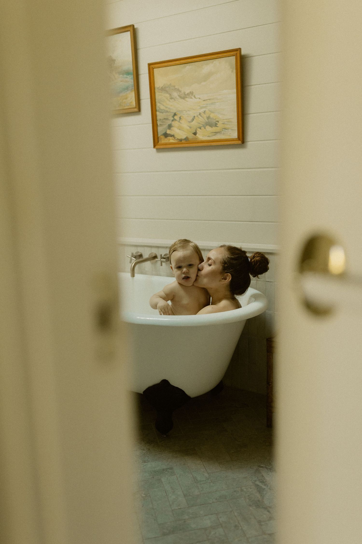 A glimpse through a doorway shows a tranquil bath scene with framed artwork on white walls.