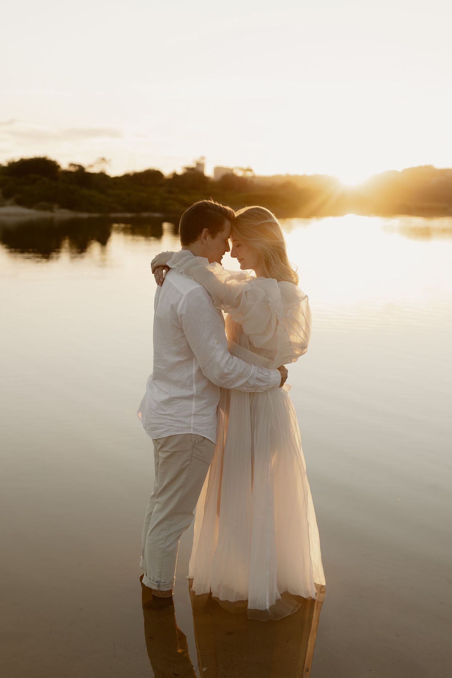 Romantic couple embraces while standing in tranquil water during golden sunset.
