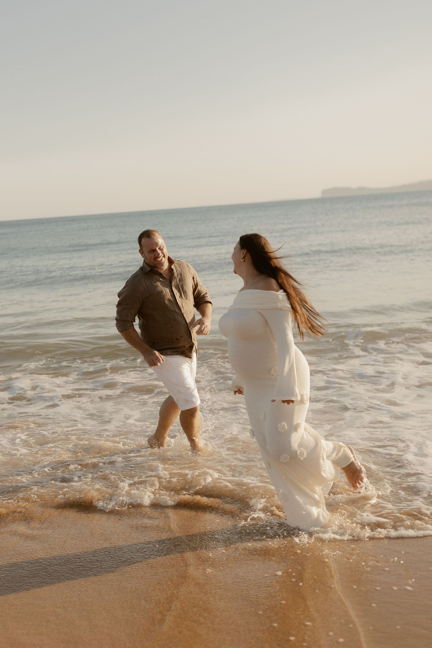 A couple dancing and splashing in the shallow ocean waves at sunset.