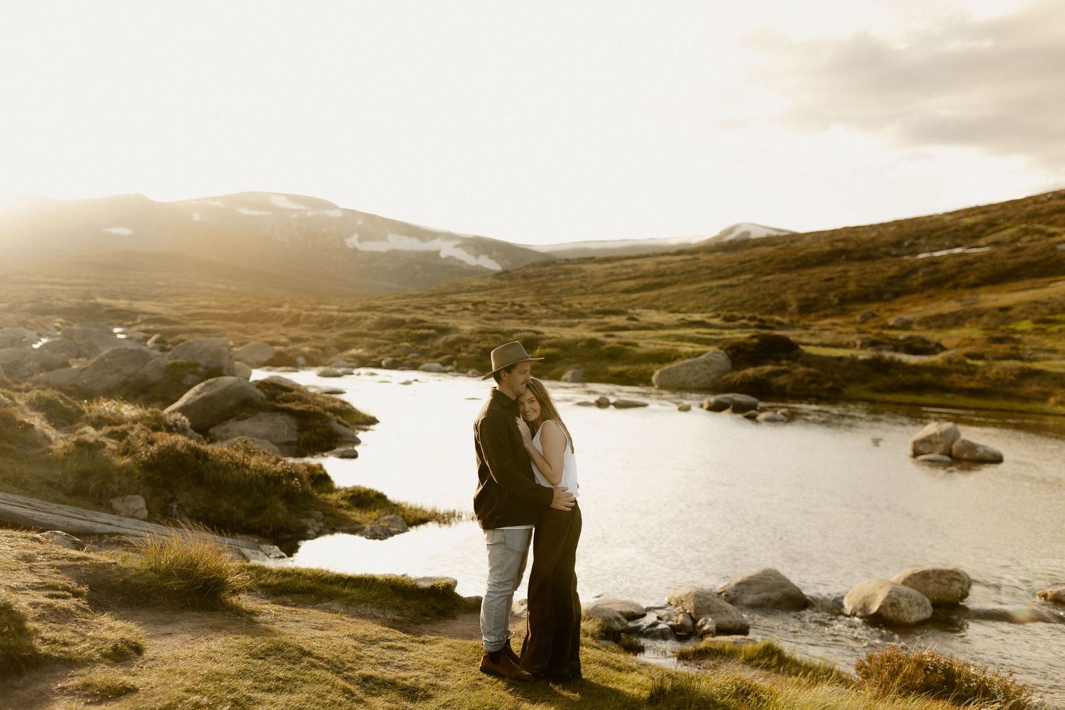 Silhouettes of two people standing on rocky coastline during golden hour with dramatic seascape backdrop.