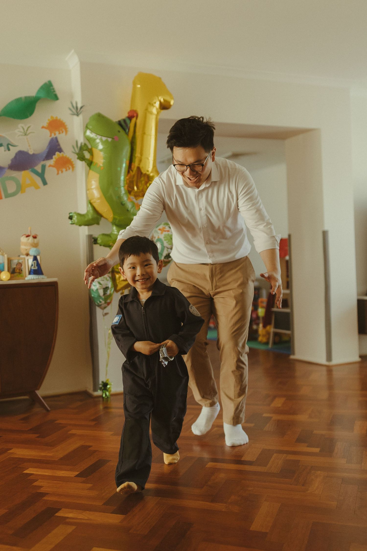 Family members play and dance together in a room decorated with colorful dinosaur balloons.