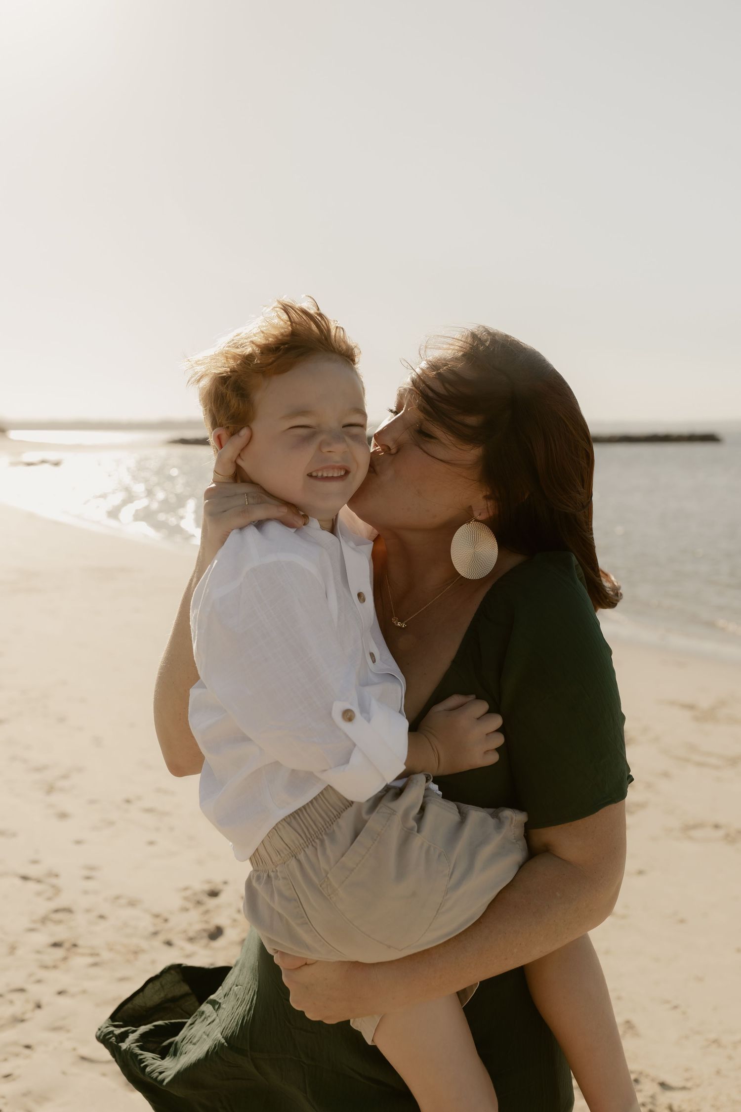 Joyful family moment captured in warm sunlight on a beach with loving embraces and laughter.