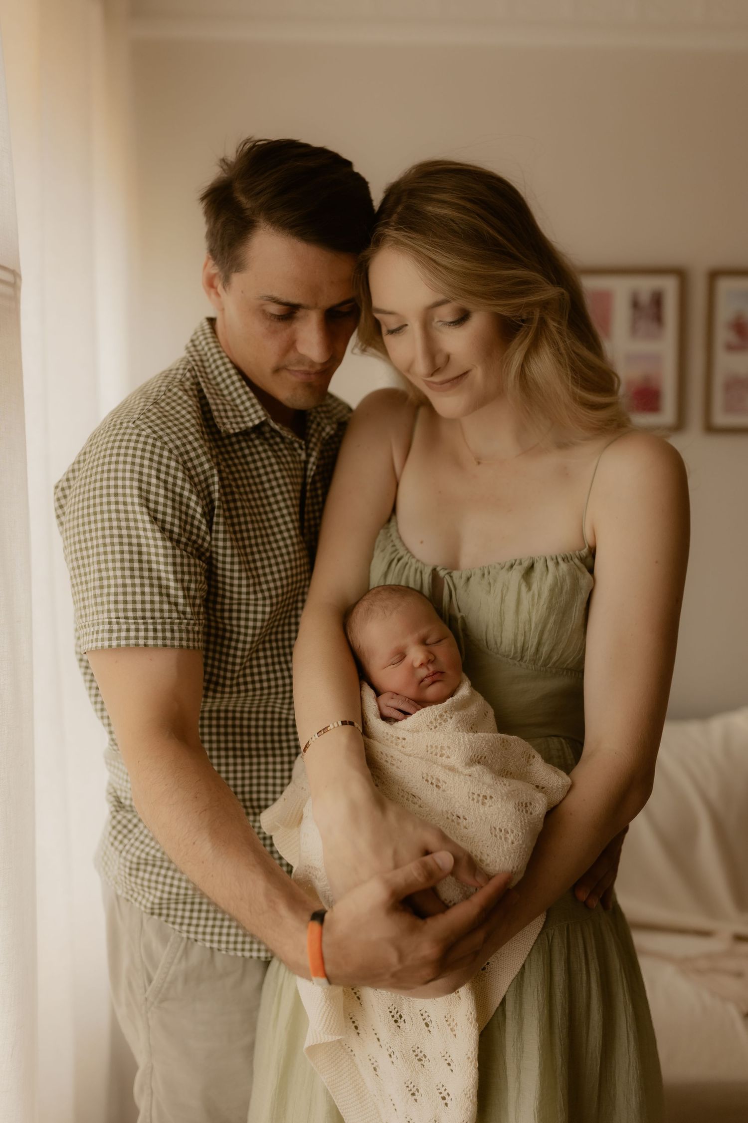 Candid lifestyle photos of parents bonding with their newborn in a sunlit room.