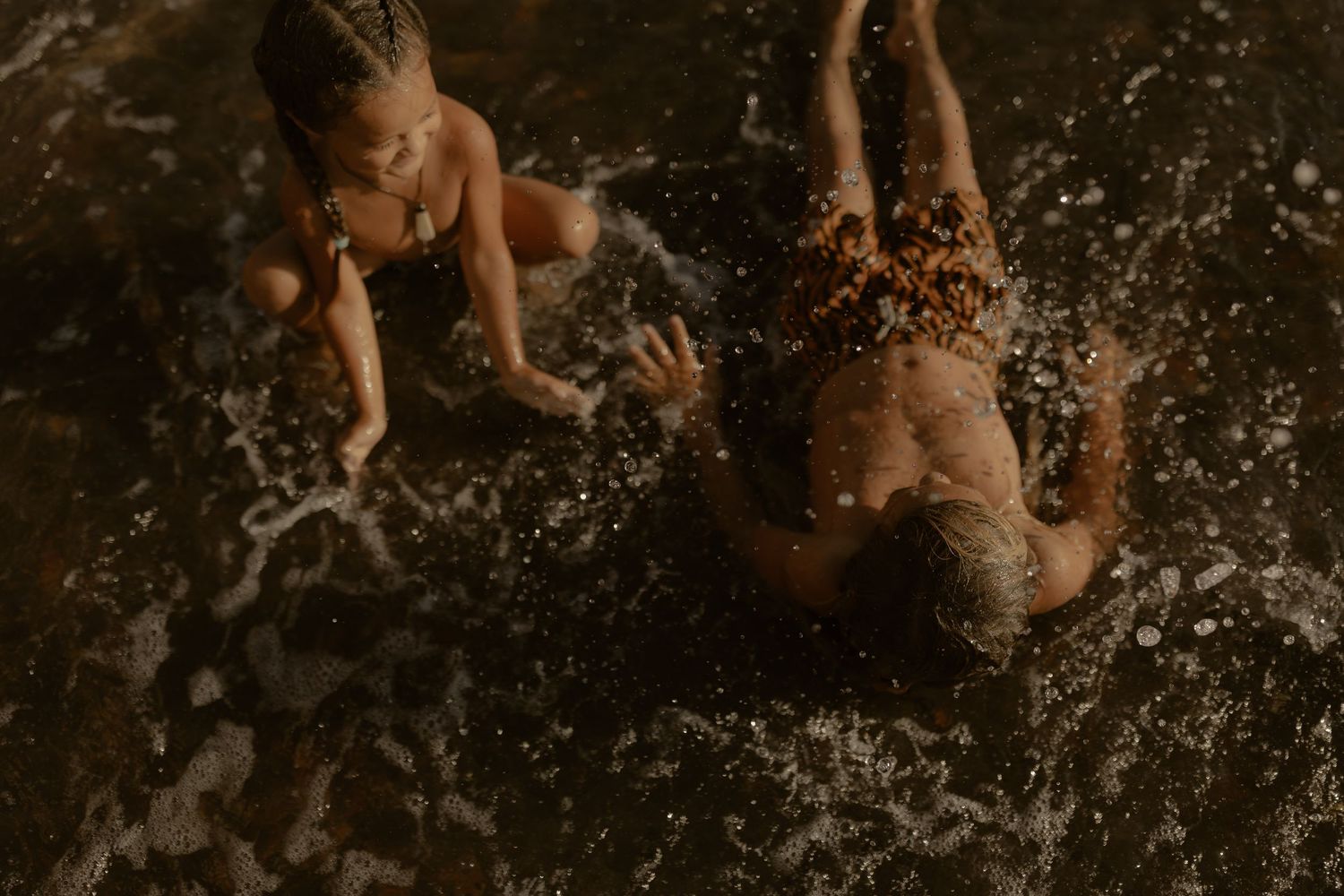 Children playing and splashing in dark water creating dramatic water droplets.