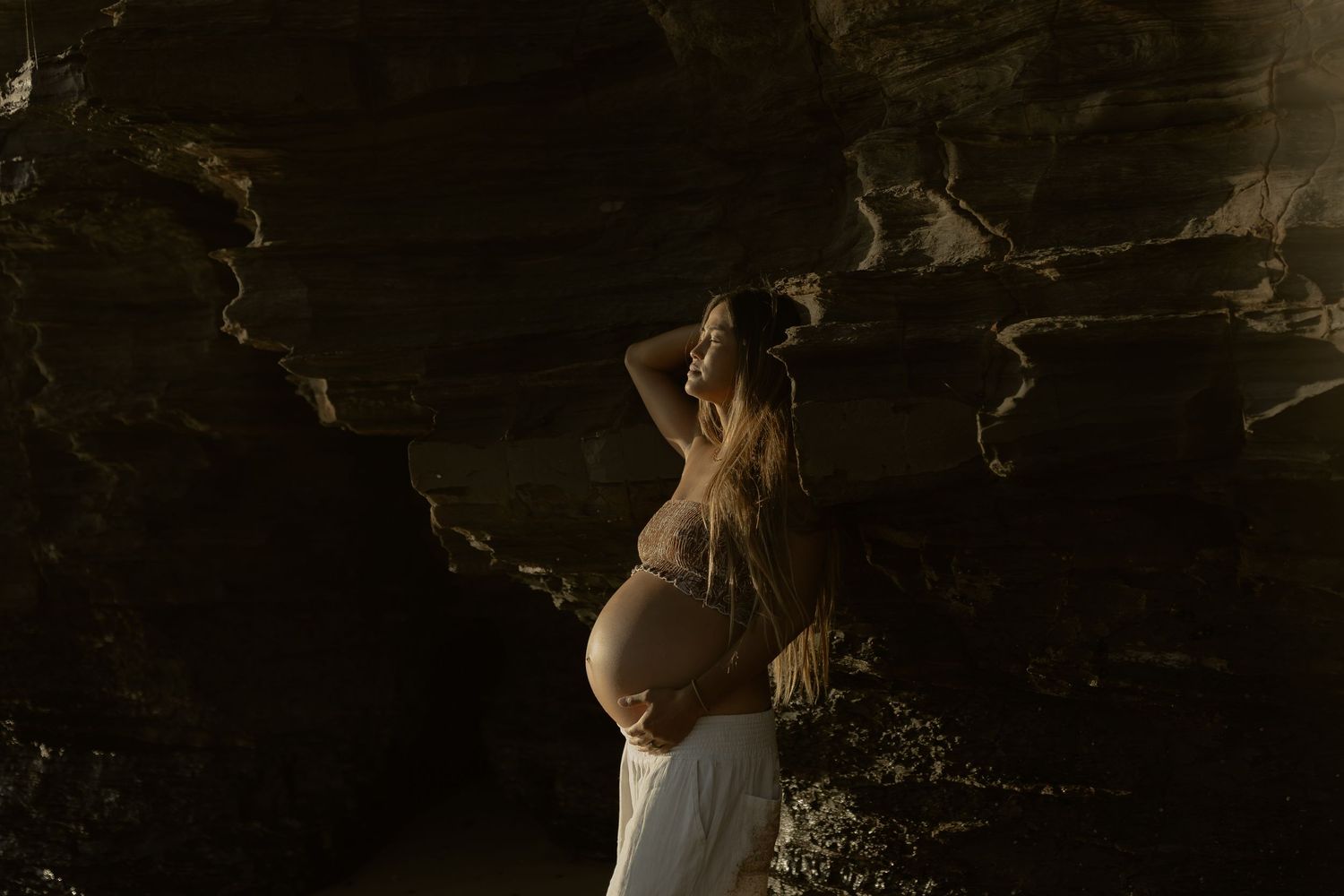 Two figures embrace on a rugged beach with towering cliffs and moody lighting in the background.