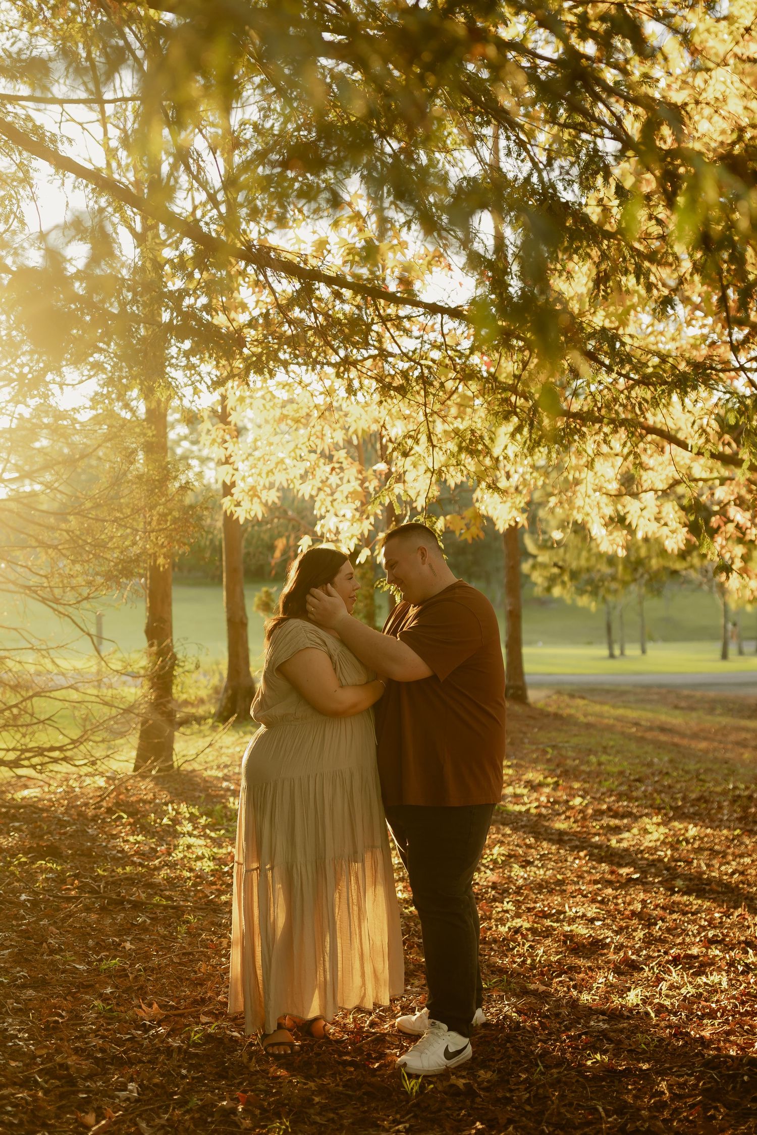 Pregnant couple sharing a tender moment under golden autumn trees in a sun-drenched park at sunset.