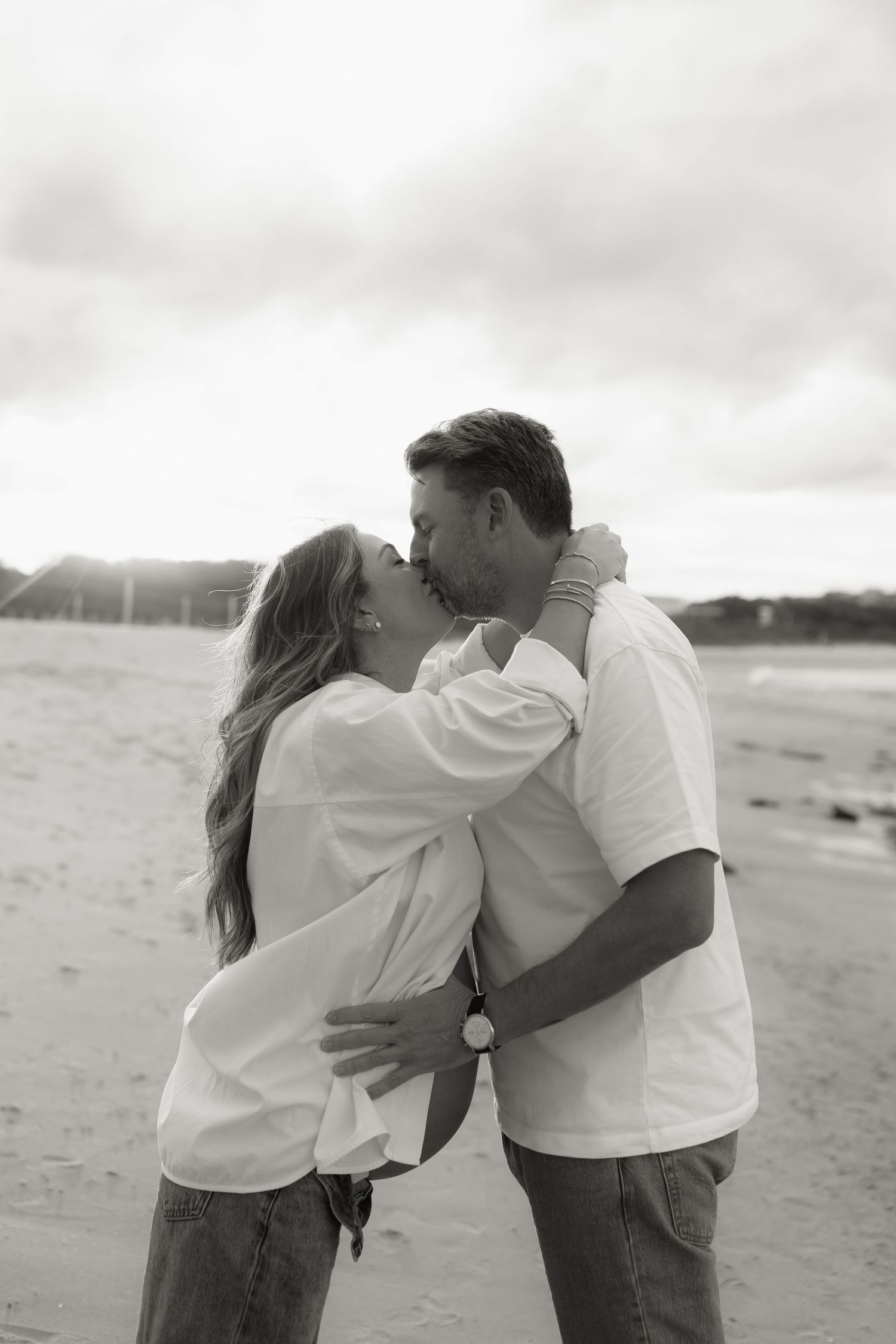 Couple kissing on beach during maternity photo shoot, black and white portrait.