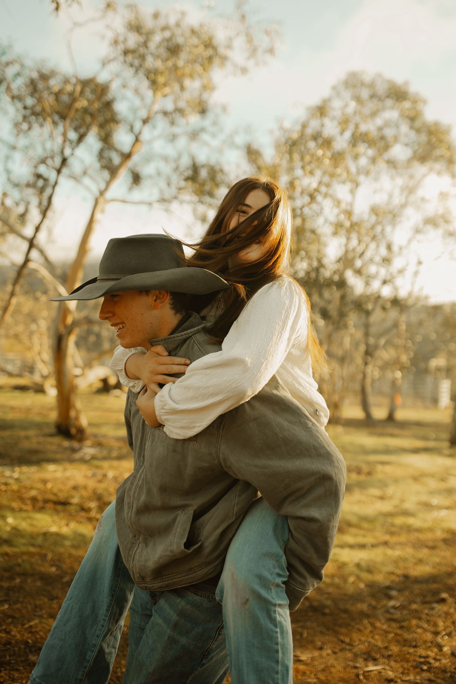 A romantic couple embracing in a rustic outdoor setting during golden hour, surrounded by autumn trees.