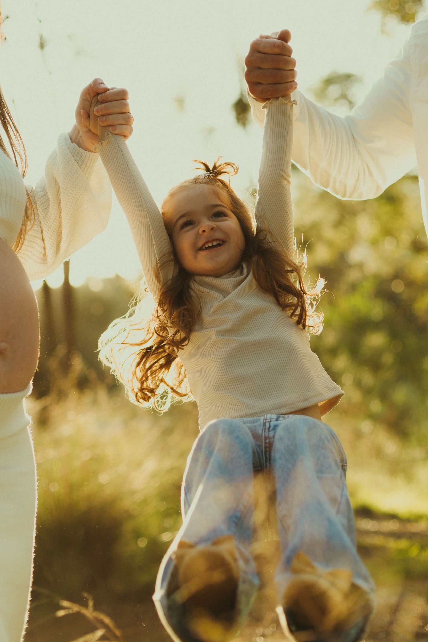 Person in white sweater and jeans jumping playfully in golden afternoon sunlight.