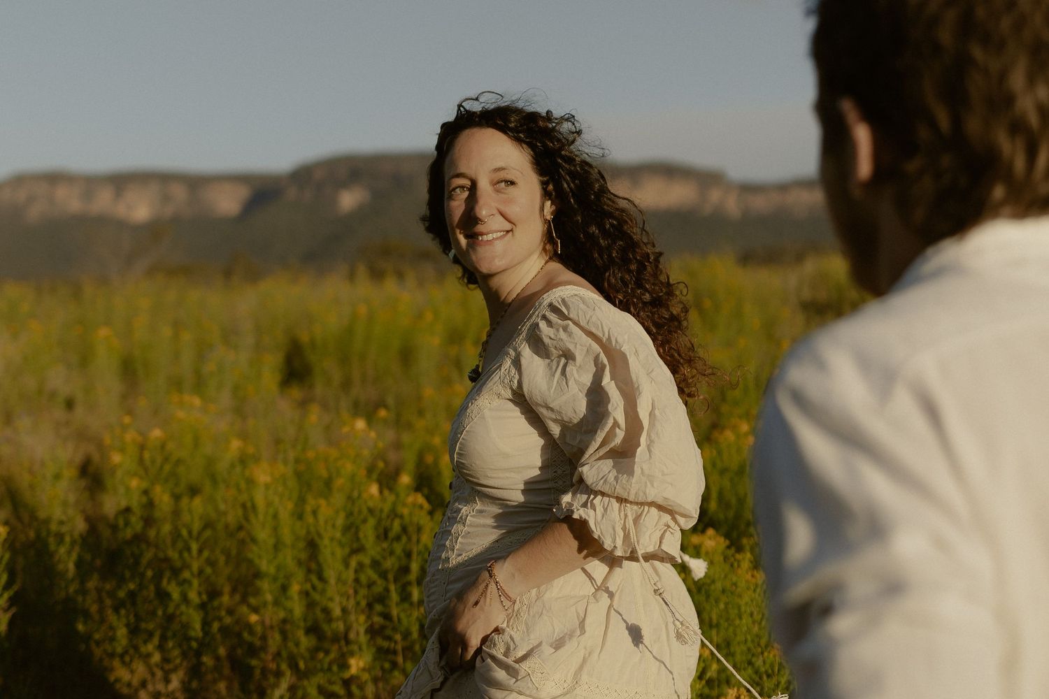 A joyful couple shares an intimate moment outdoors against a natural landscape with mountains in the background.
