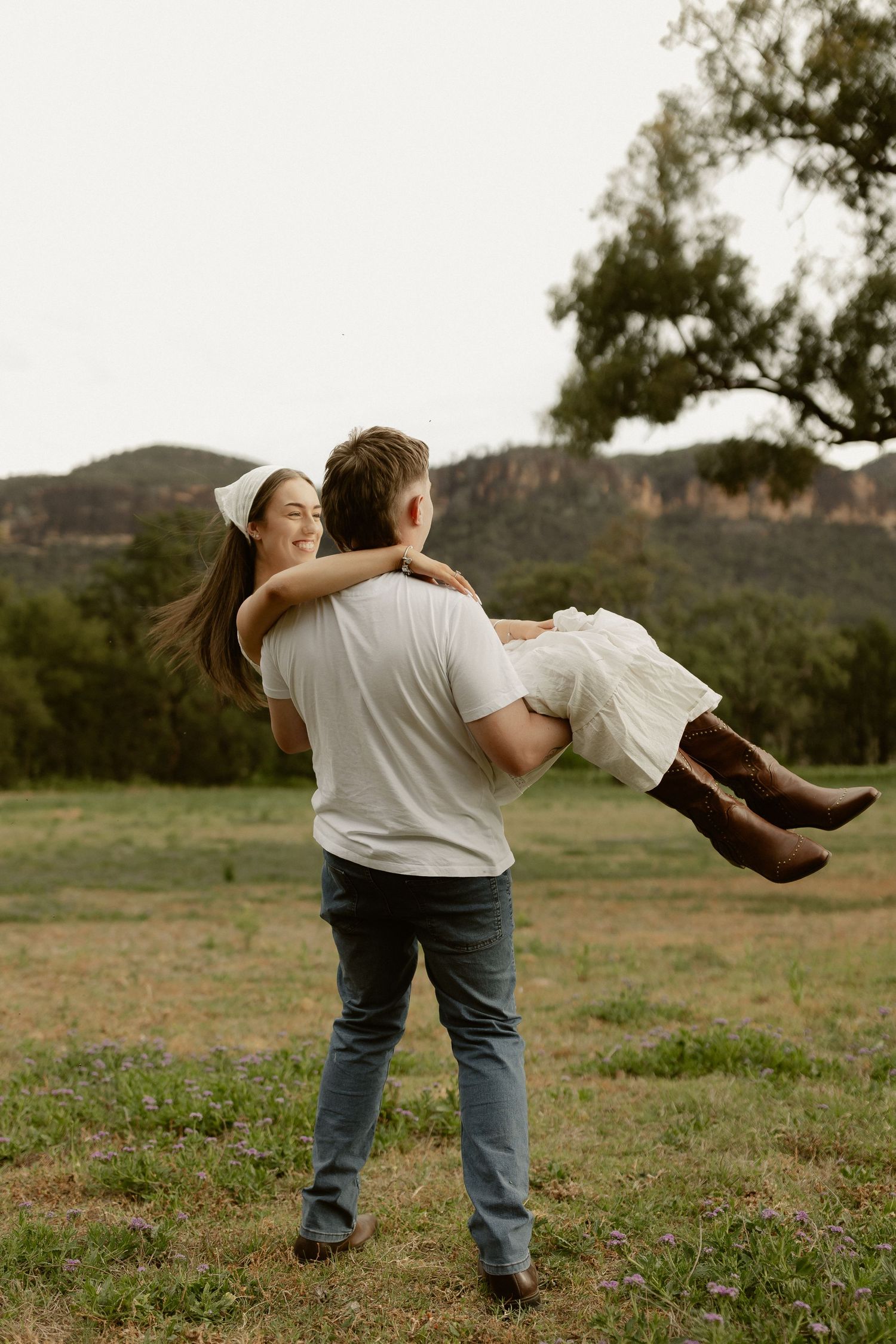 A couple in casual attire spins and dances together in a grassy field.