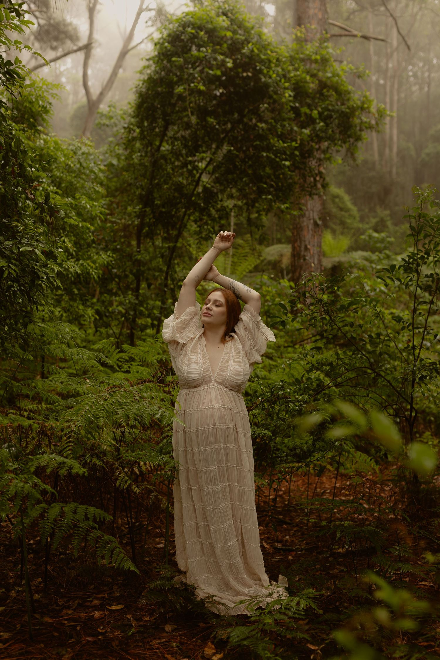 Figure in flowing vintage dress dances gracefully among lush green forest foliage.