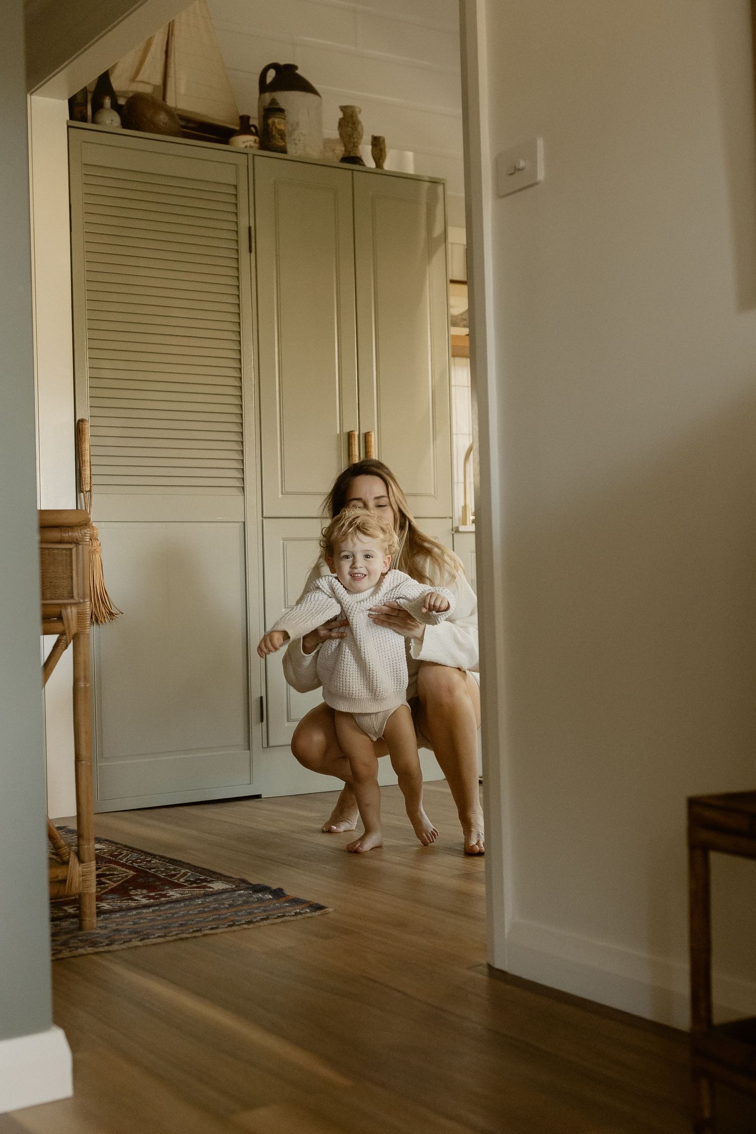 Two people in white outfits share a joyful moment dancing and playing together in a sunlit room with hardwood floors.
