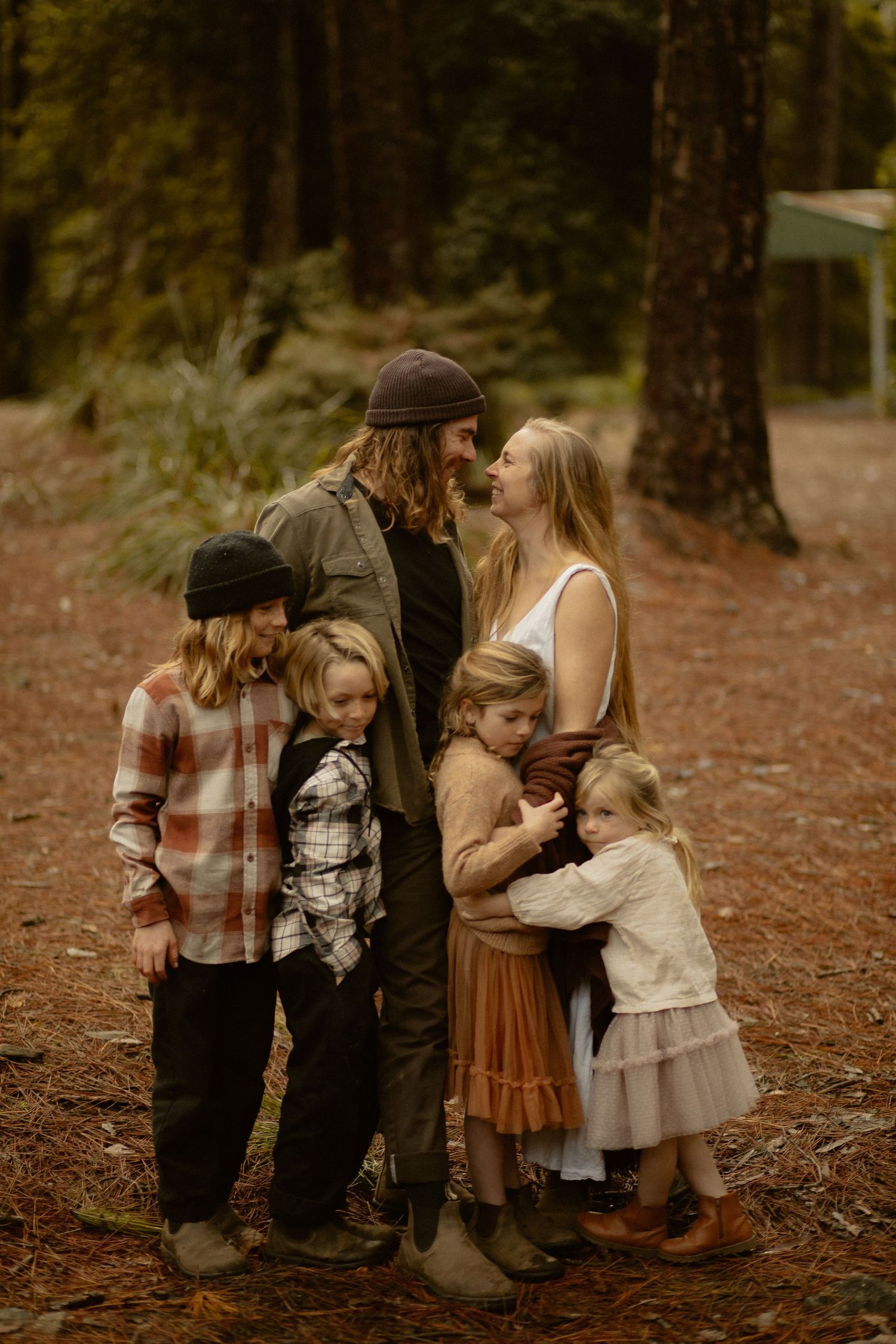 Tender family moment photographed in warm autumn light within a pine forest setting.