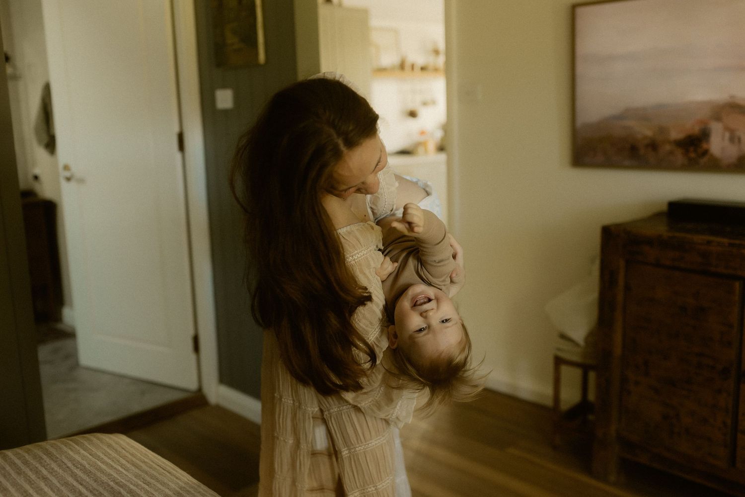 Sweet nurturing moment captured in natural light with wooden furniture and white walls.