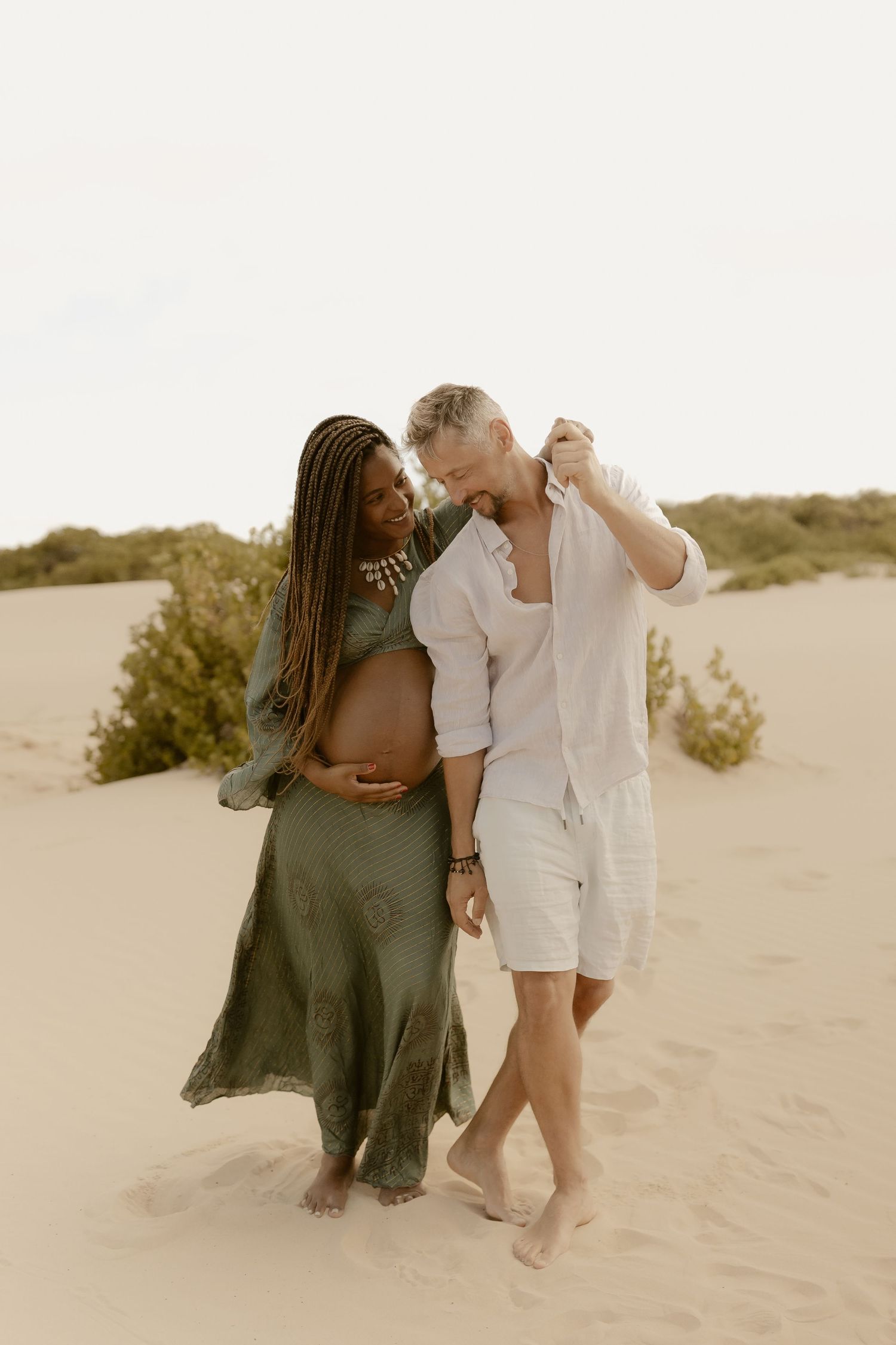 A romantic couple embraces on sandy dunes during a desert photoshoot at sunset.