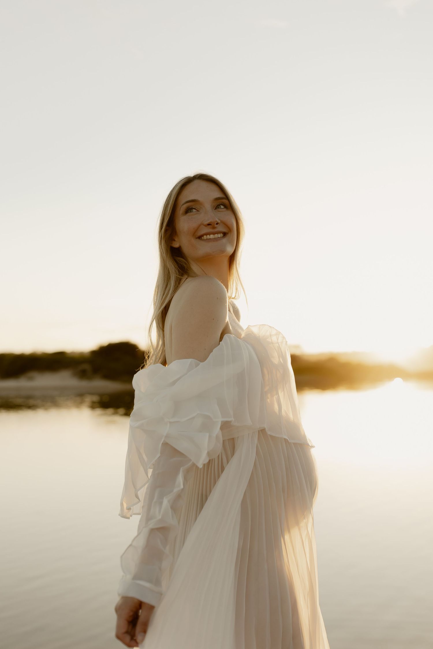 Dreamy lakeside scene with a figure in white ruffled dress gazing upward during sunset.