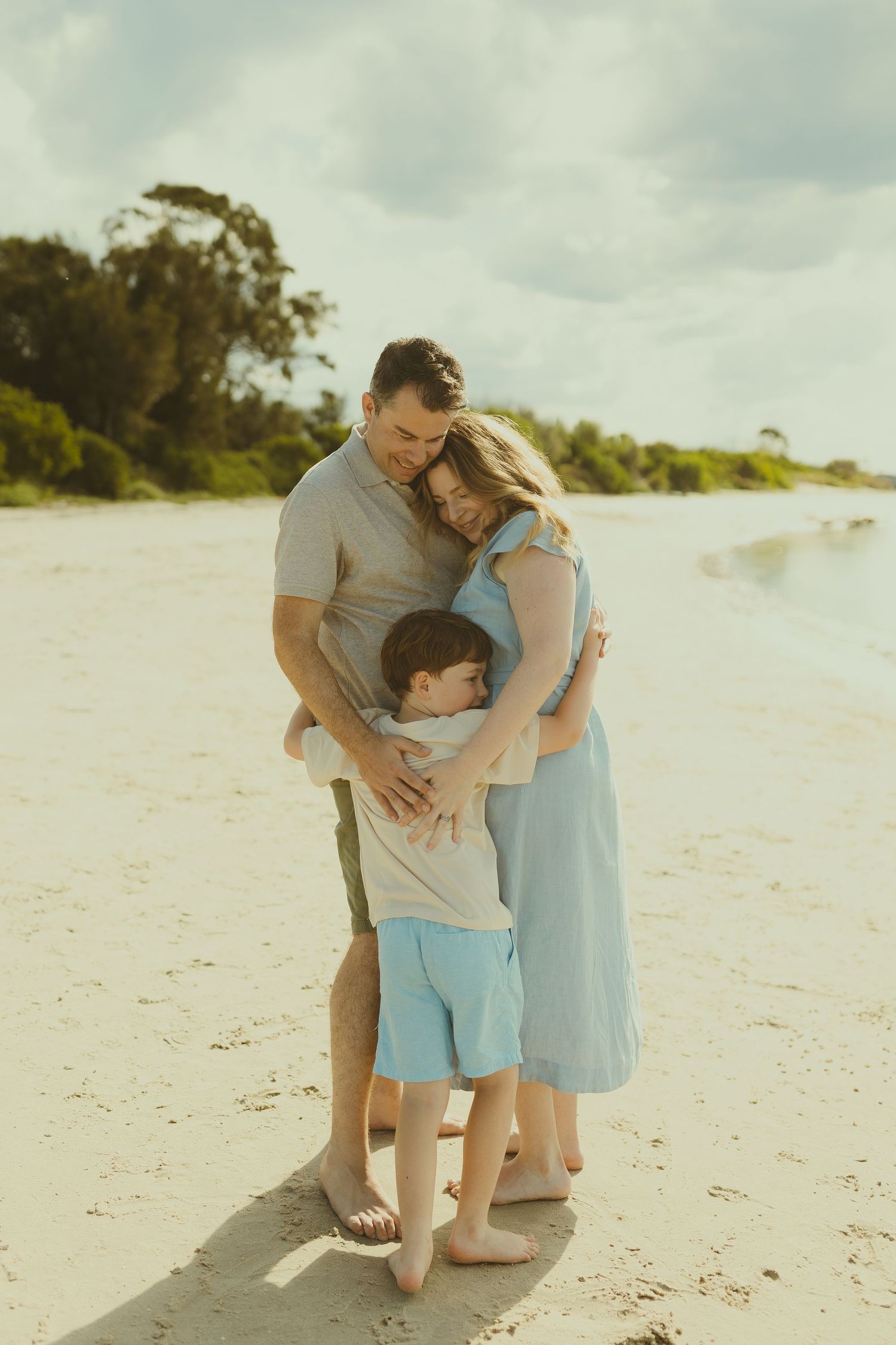 A family shares tender moments together while walking along a pristine white sandy beach on a cloudy day.