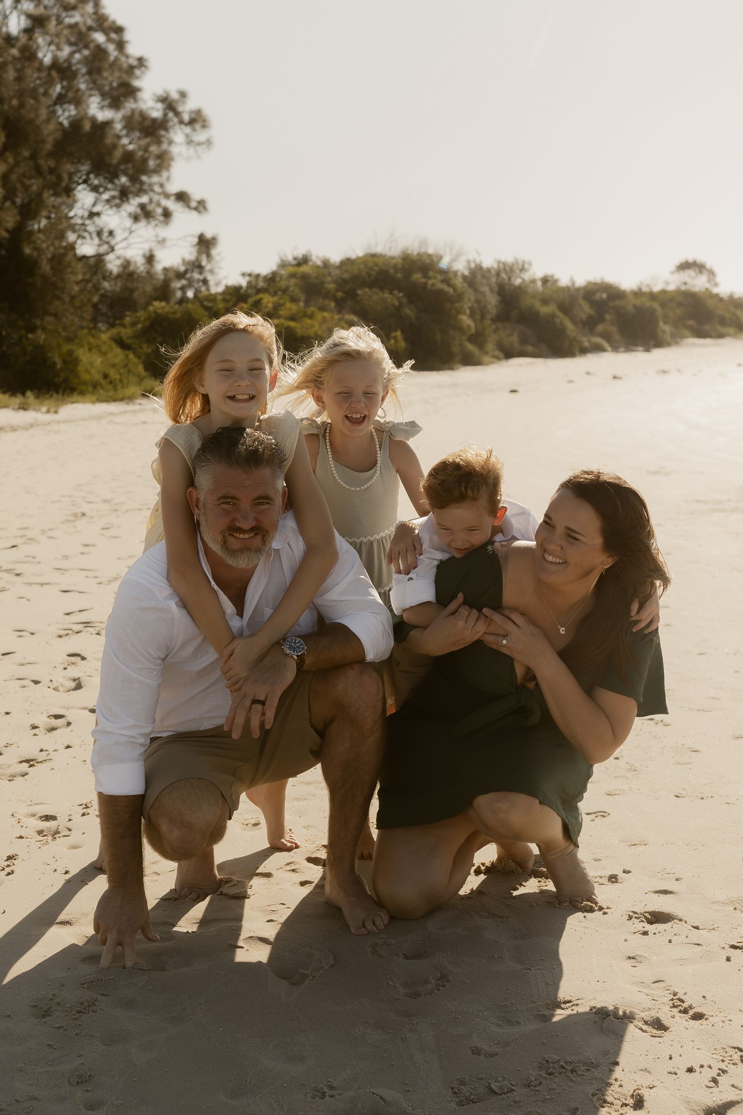 A group of friends laughing together while crouching on a sandy beach at sunset.