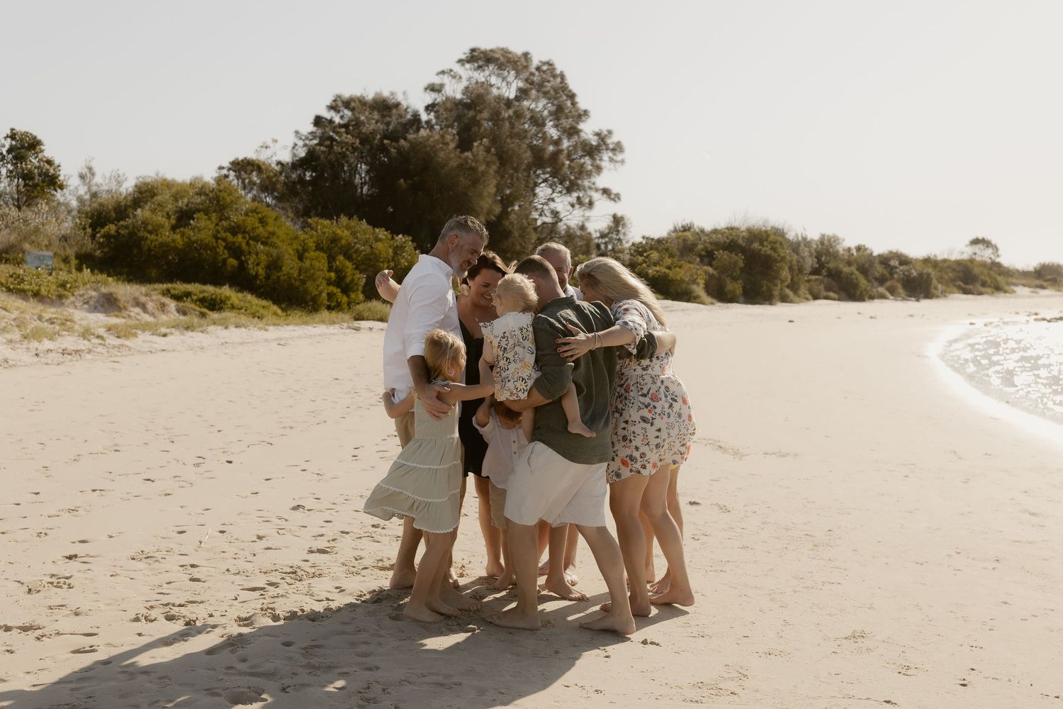Family enjoying a serene moment together on a sunny beach with natural coastal scenery in the background.