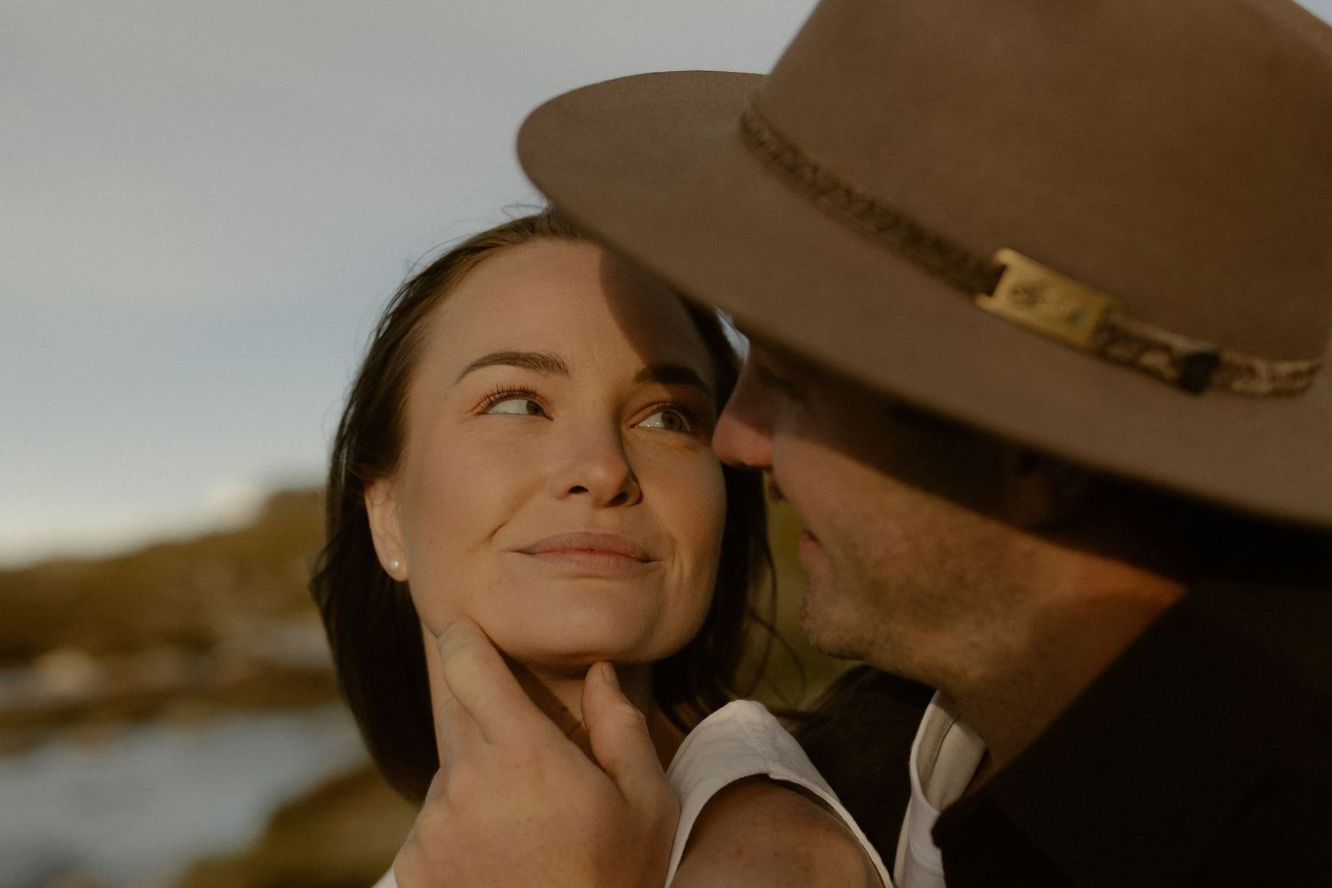 A romantic couple embraces outdoors during golden hour while wearing western-style attire.