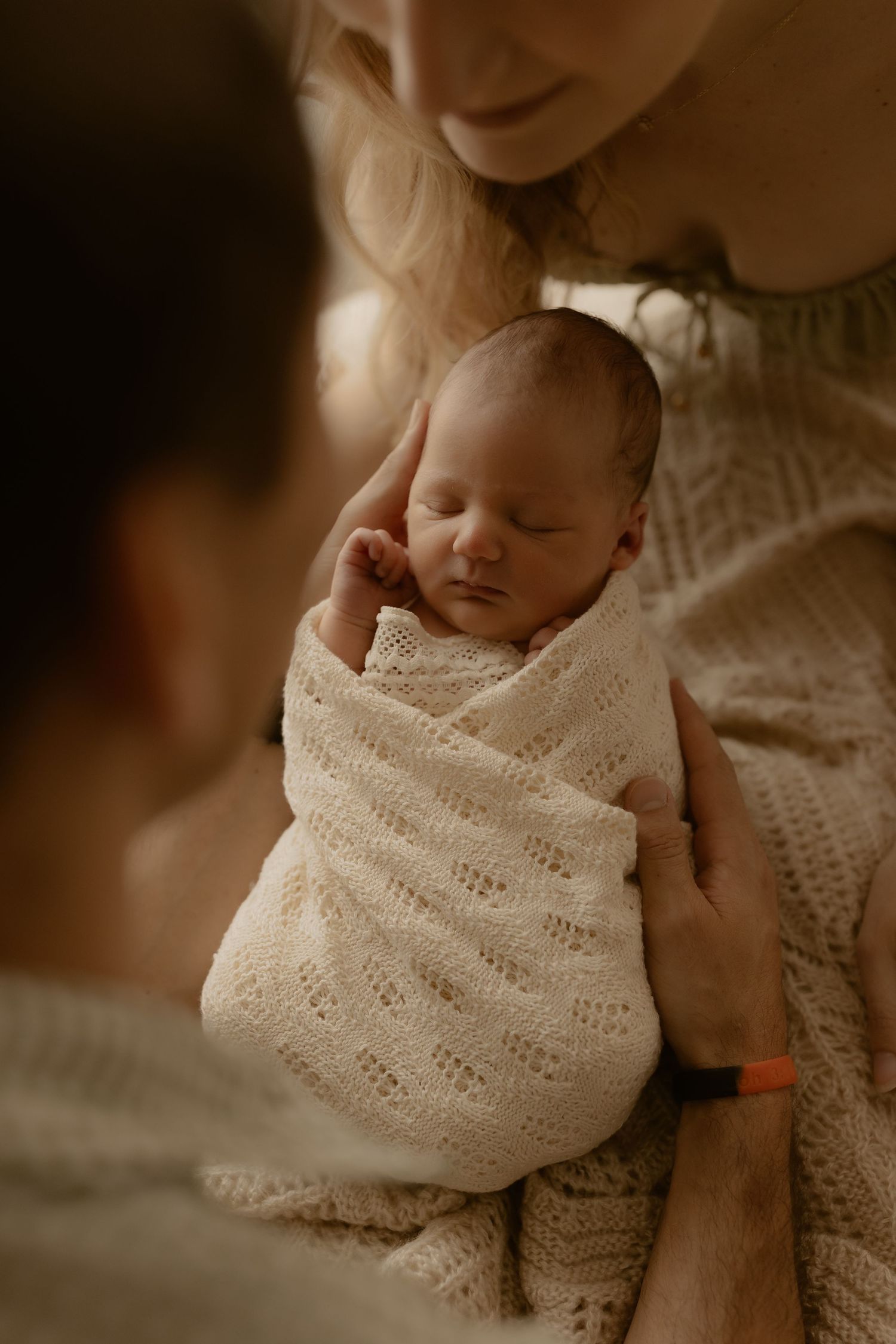 Sleeping newborn wrapped in delicate white knit blanket creating peaceful nursery scene.