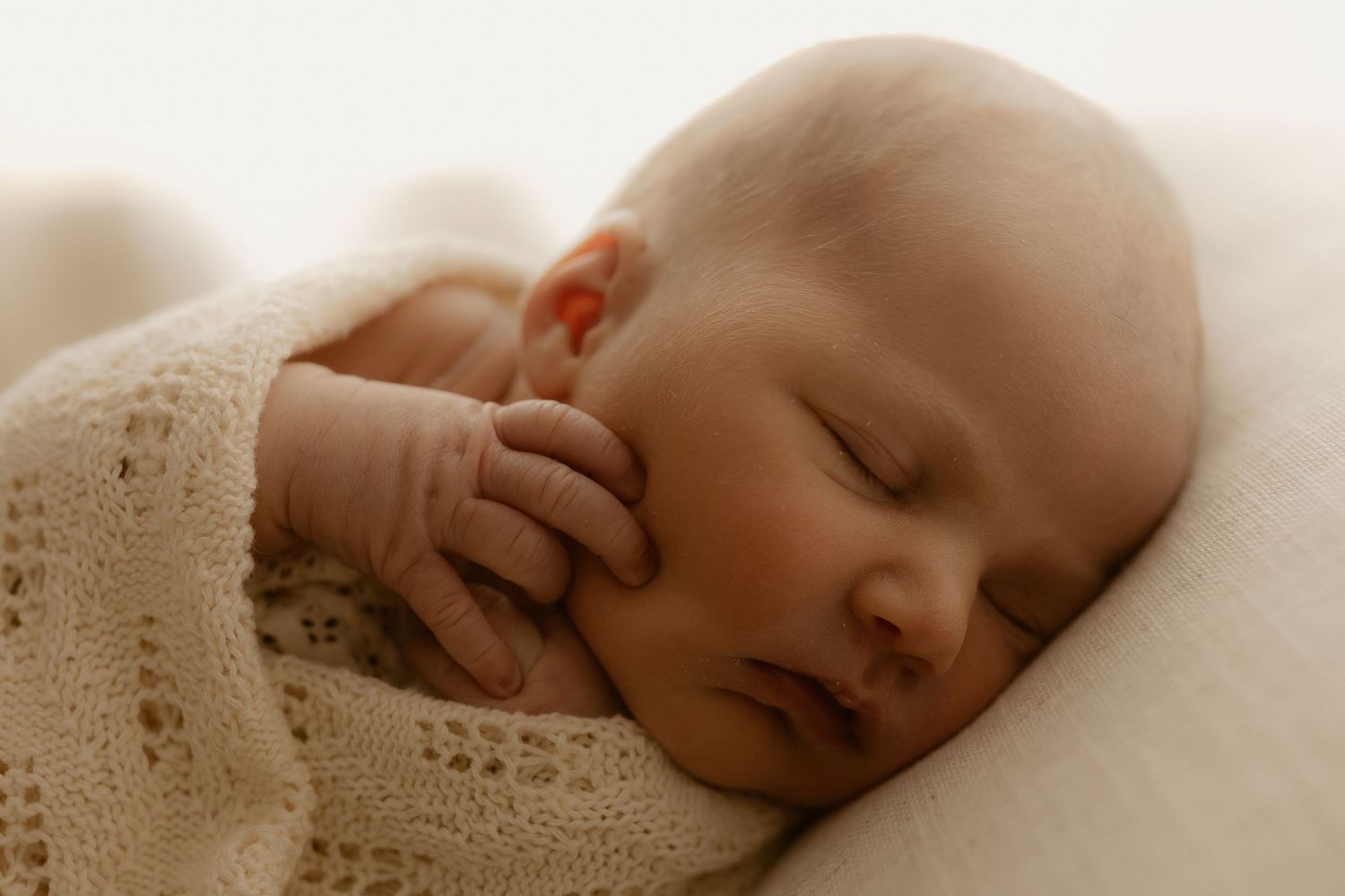 A peaceful sleeping baby wrapped in soft cream-colored knit blankets rests in a serene pose.