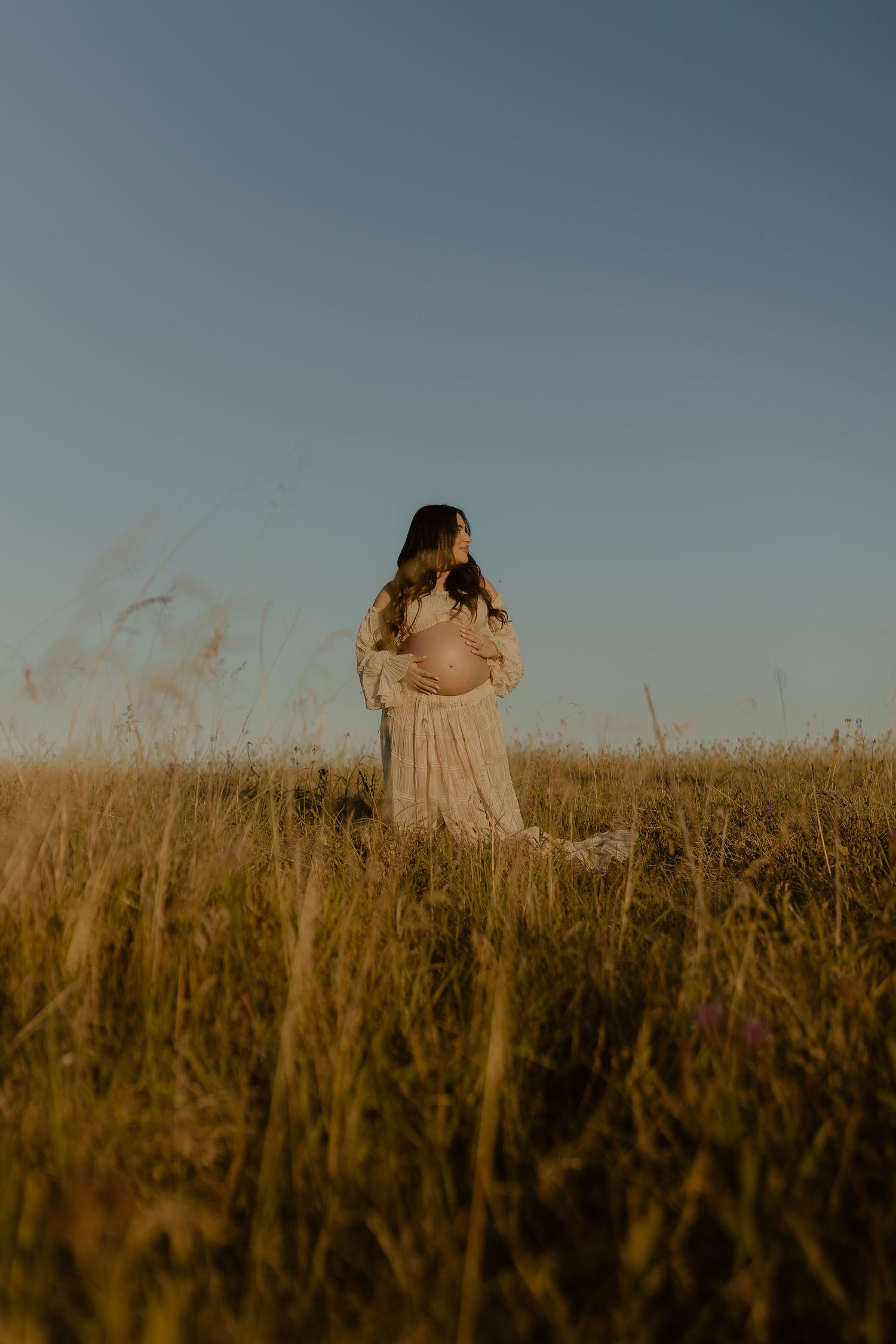 Couple embraces in golden wheat field during sunset creating romantic silhouettes against the sky.