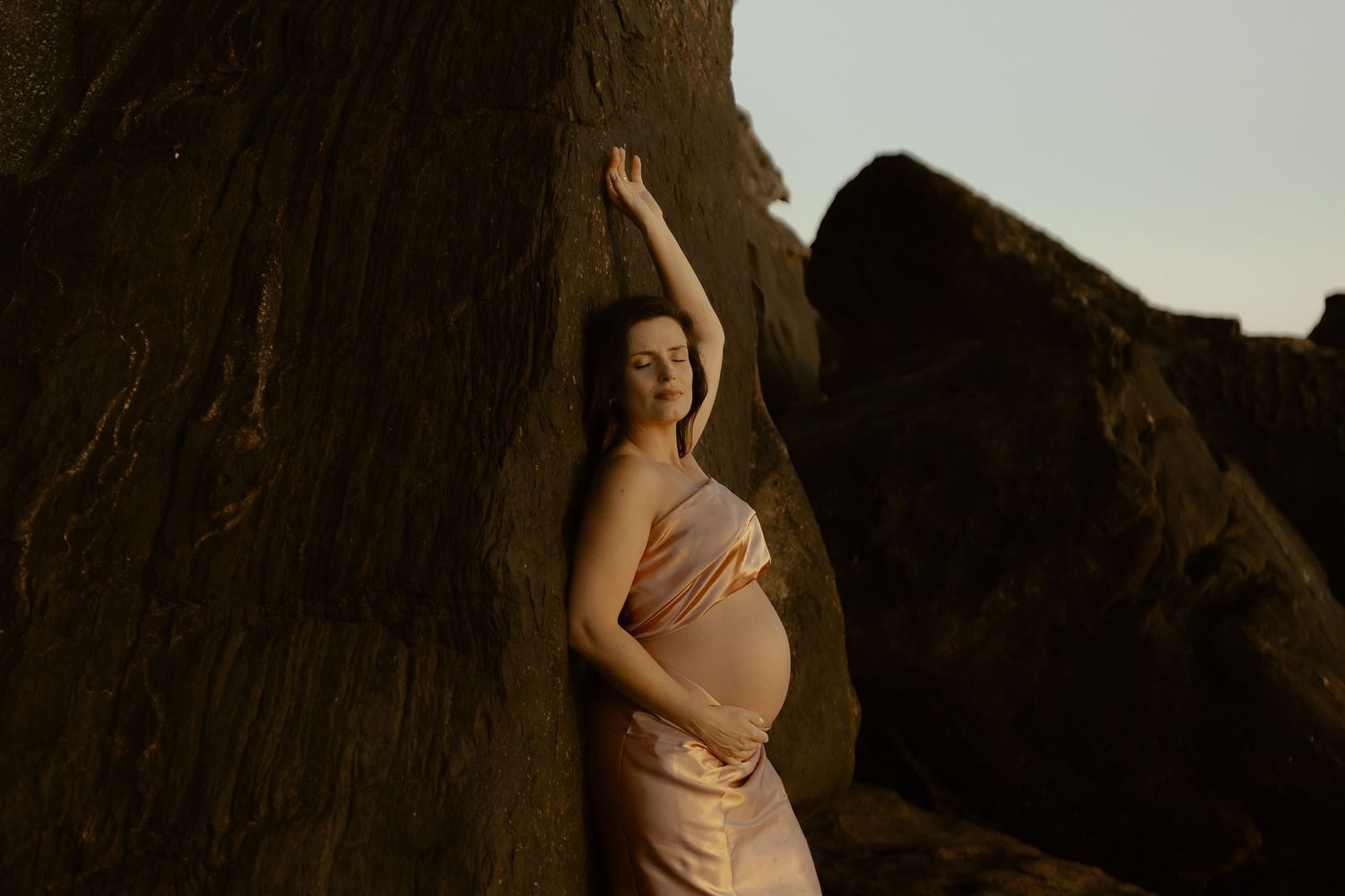A figure in a white dress poses against dramatic rock formations at sunset creating a silhouetted effect.