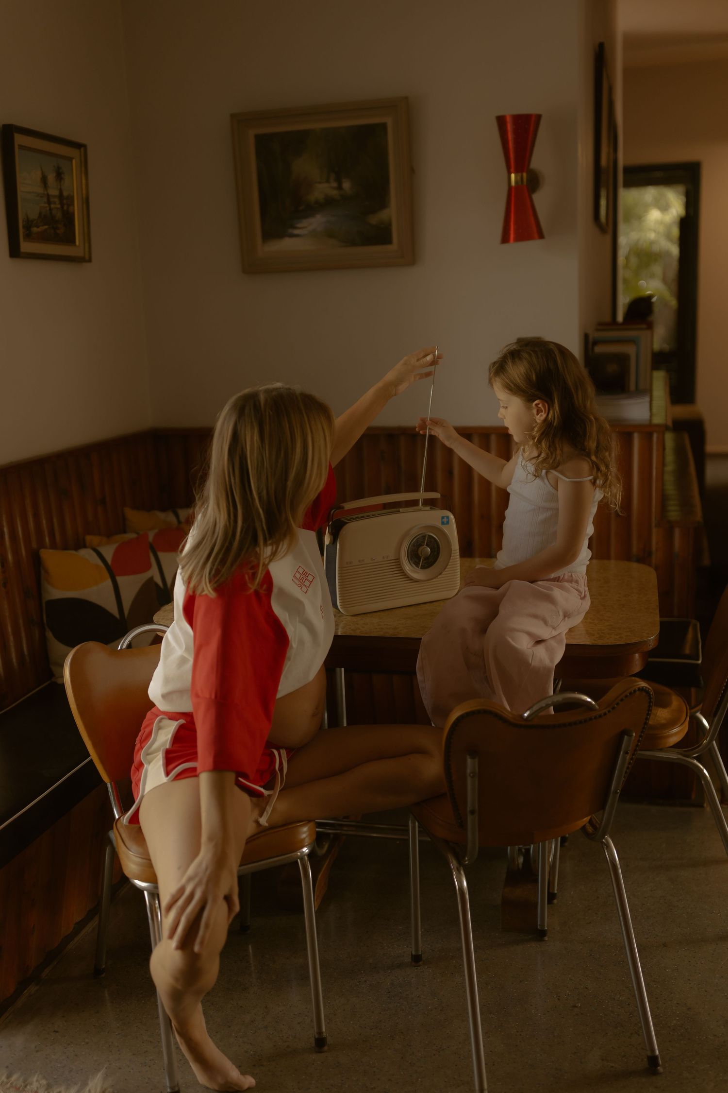 Young girl and woman interact with a vintage radio in a retro-styled living room.
