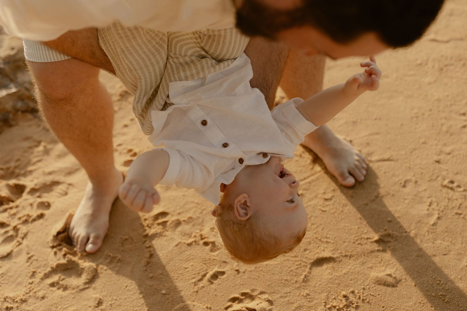 Close-up view of tiny feet and hands making imprints in smooth beach sand on a bright day.