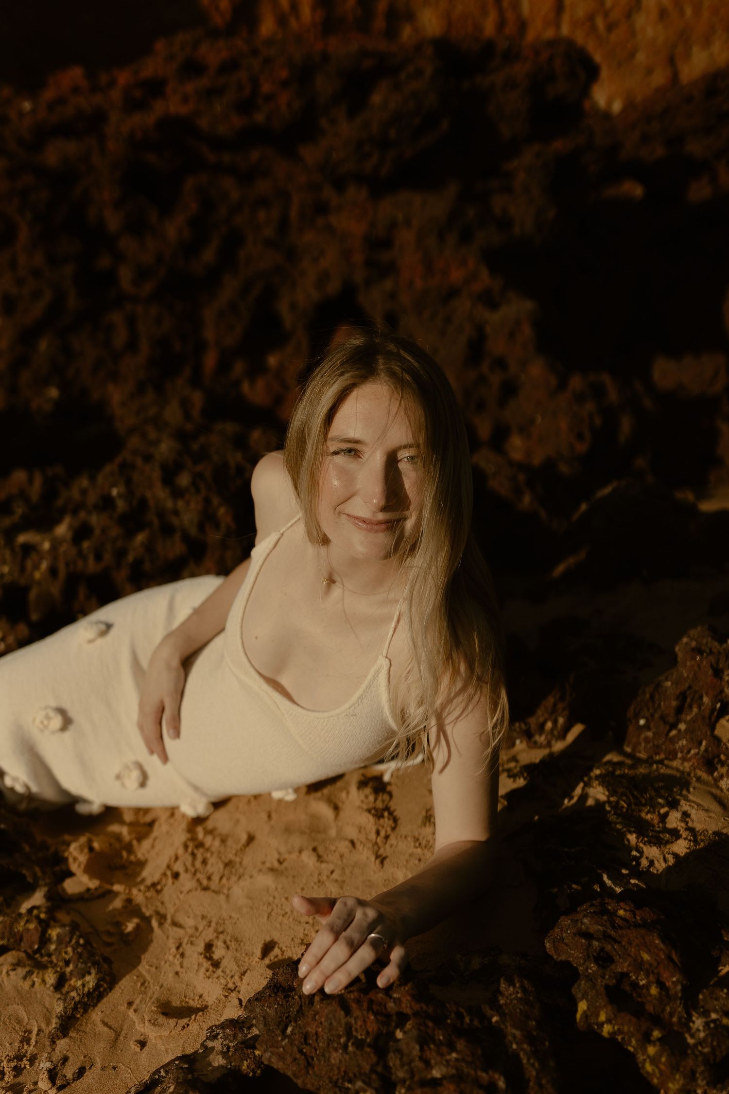 A person in a white top poses against rocky terrain in warm lighting.