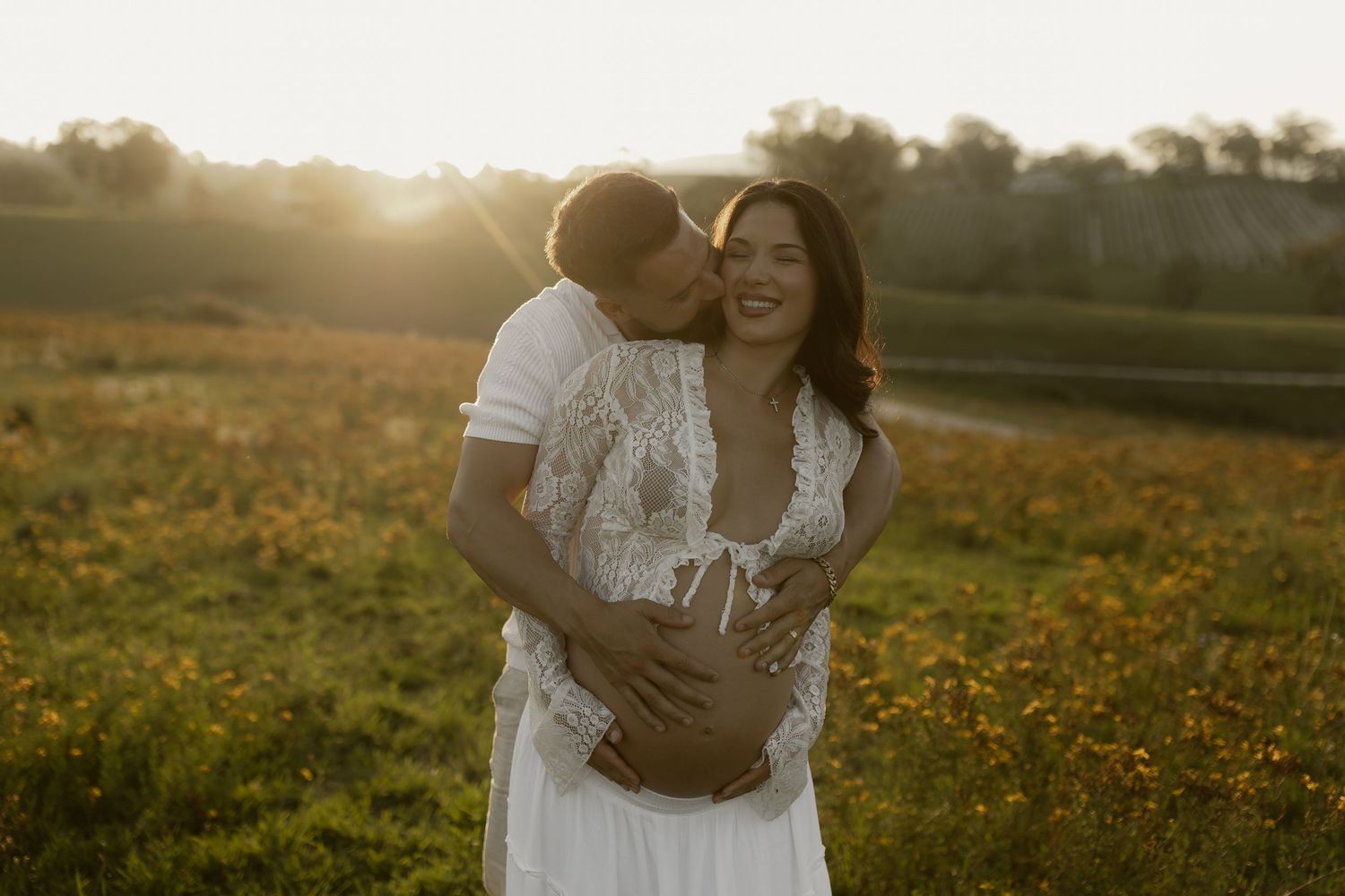 Couple shares intimate embrace in golden field during sunset photoshoot.