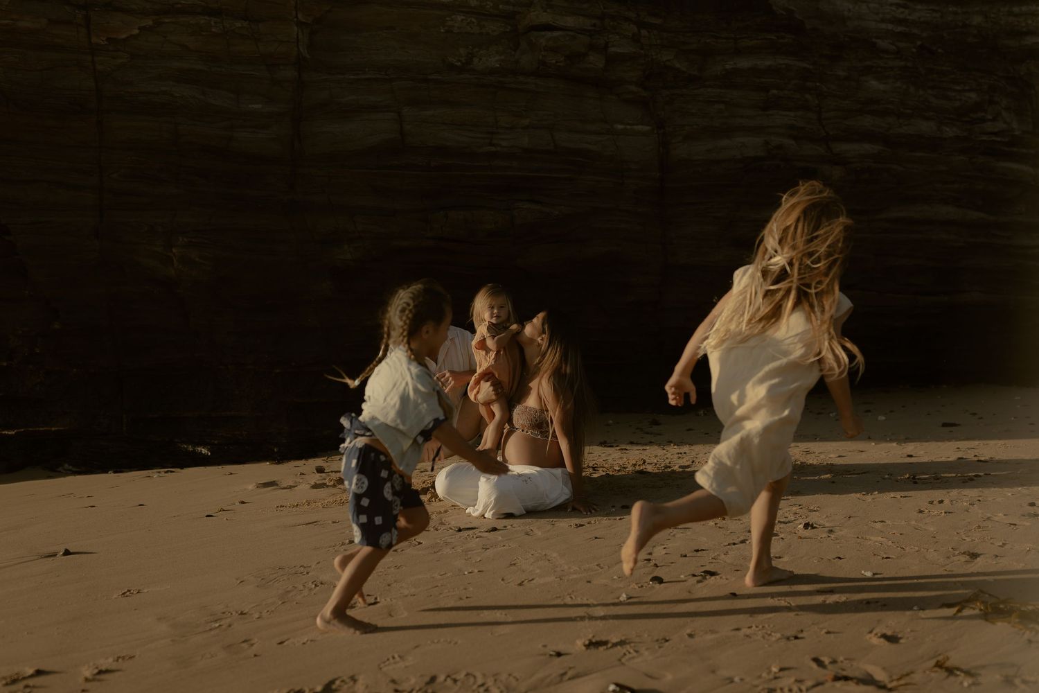 Children playing and running freely on a beach near rocky cliffs at golden hour.