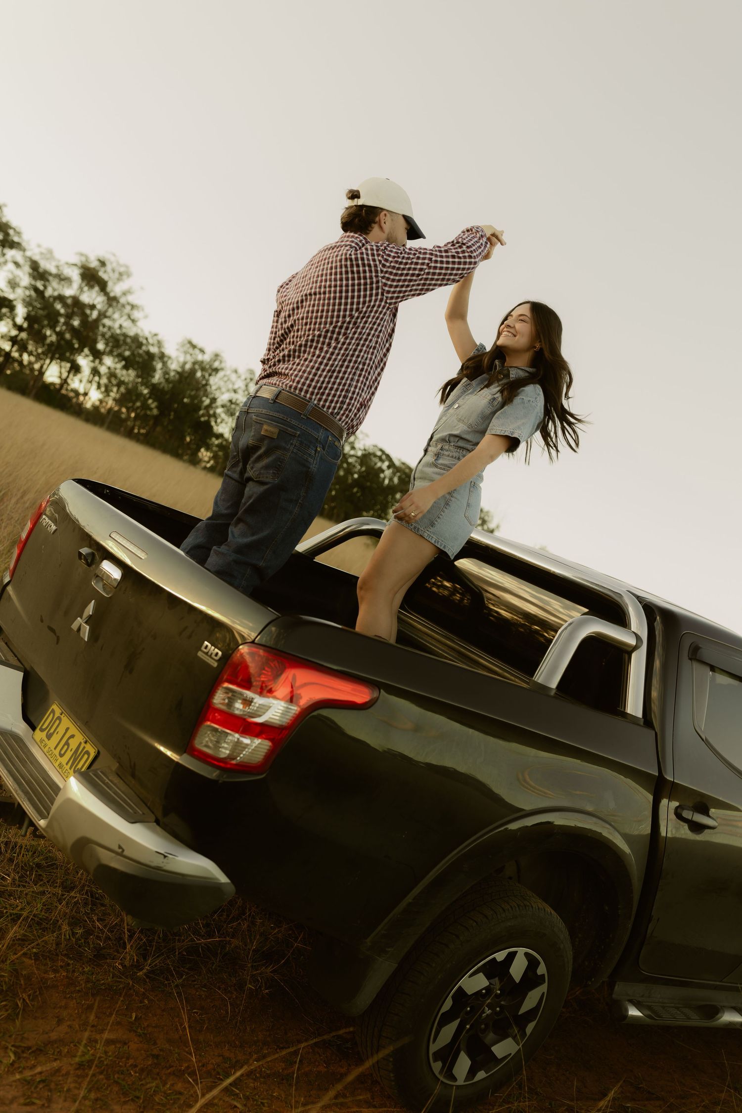 A couple dancing on the bed of a black Mitsubishi pickup truck in a rural outdoor setting.