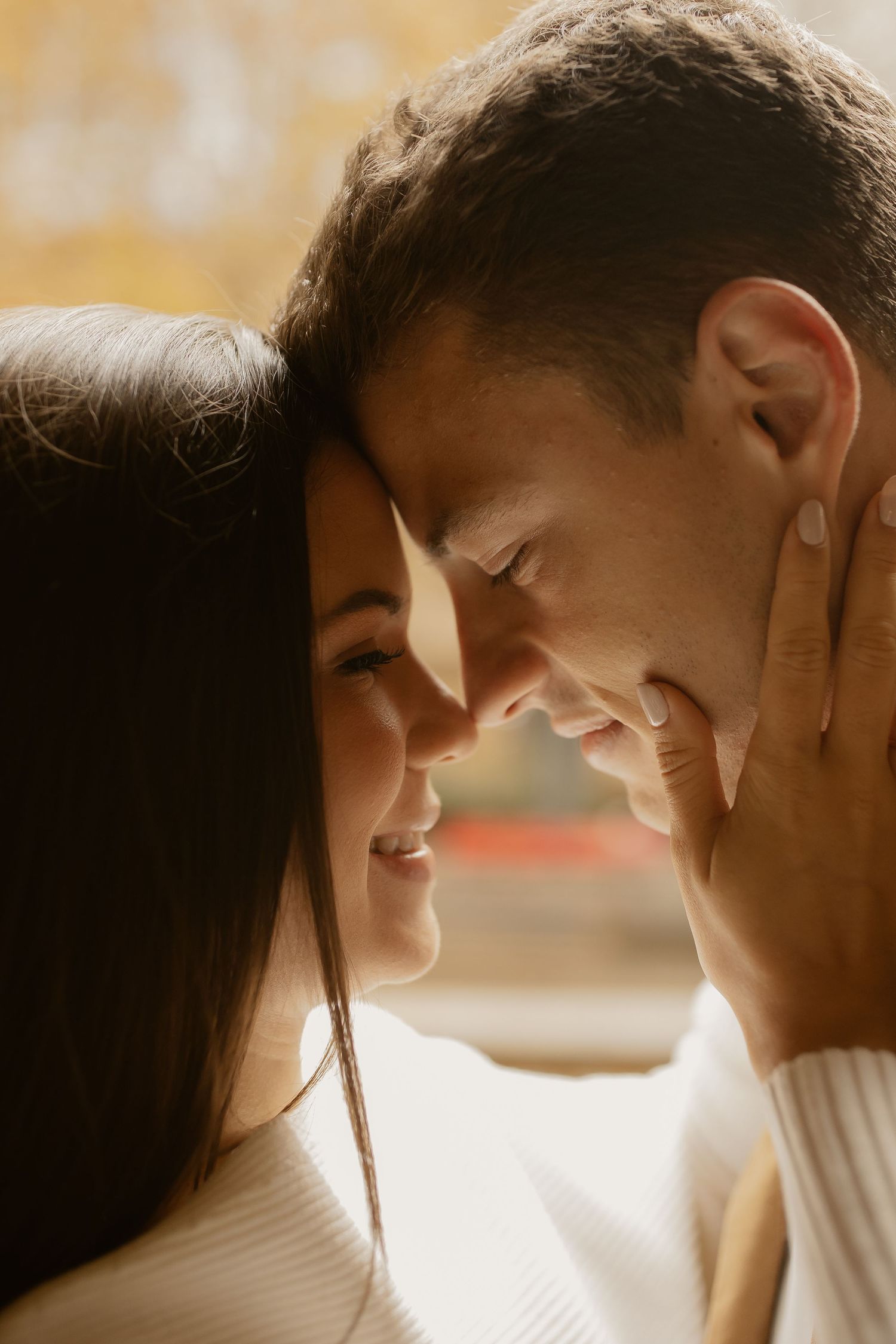 A romantic couple in white sweaters share an intimate moment in warm sunlight.