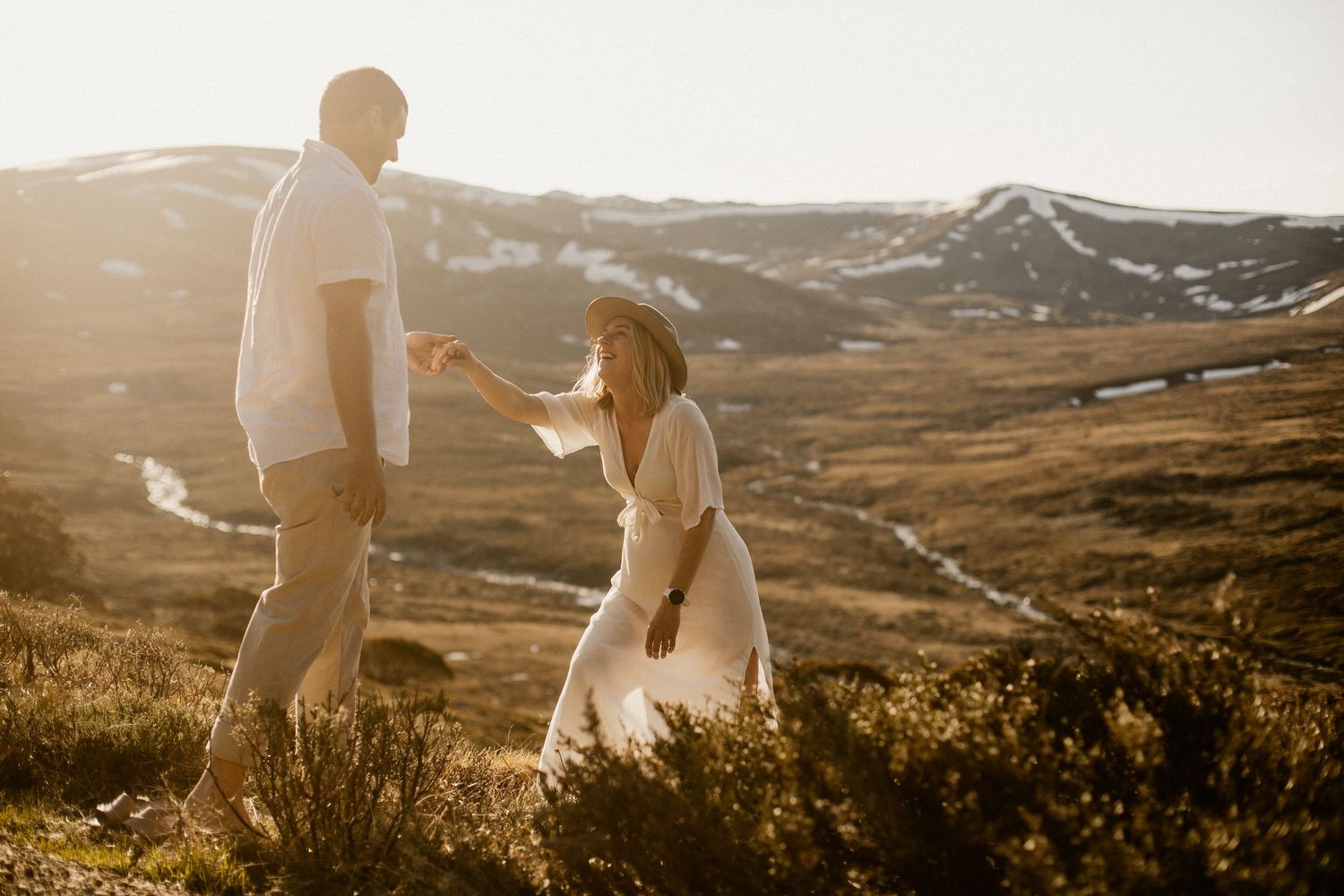 A couple shares an intimate moment during golden hour on a mountain ridge overlooking scenic rolling hills.