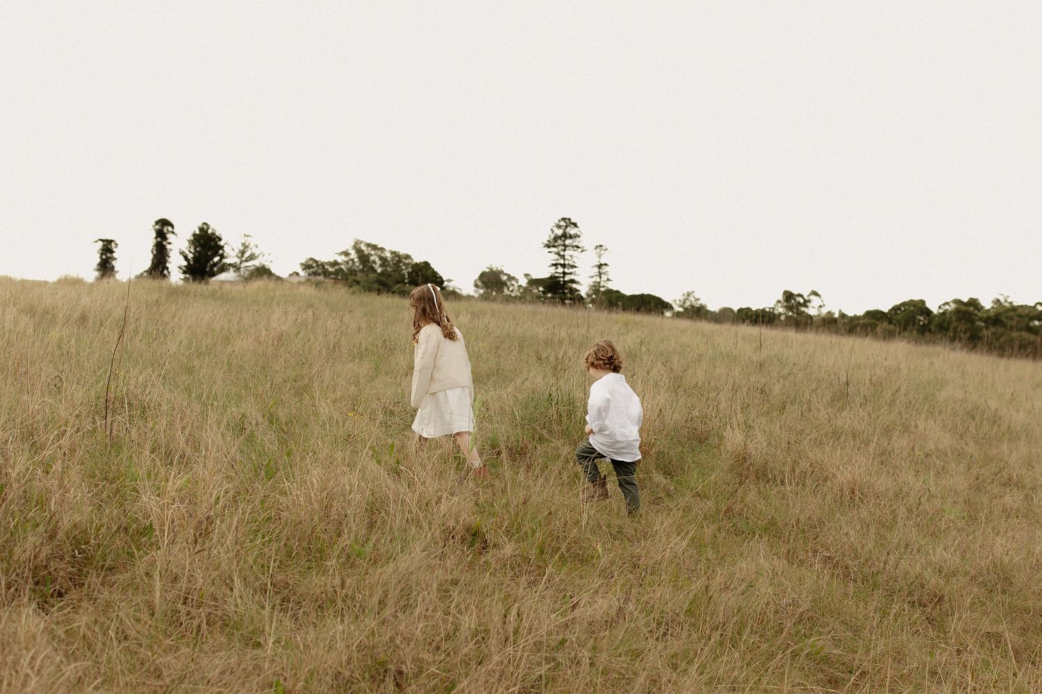 People wearing light colored clothing stroll through a sunlit meadow on a warm afternoon.