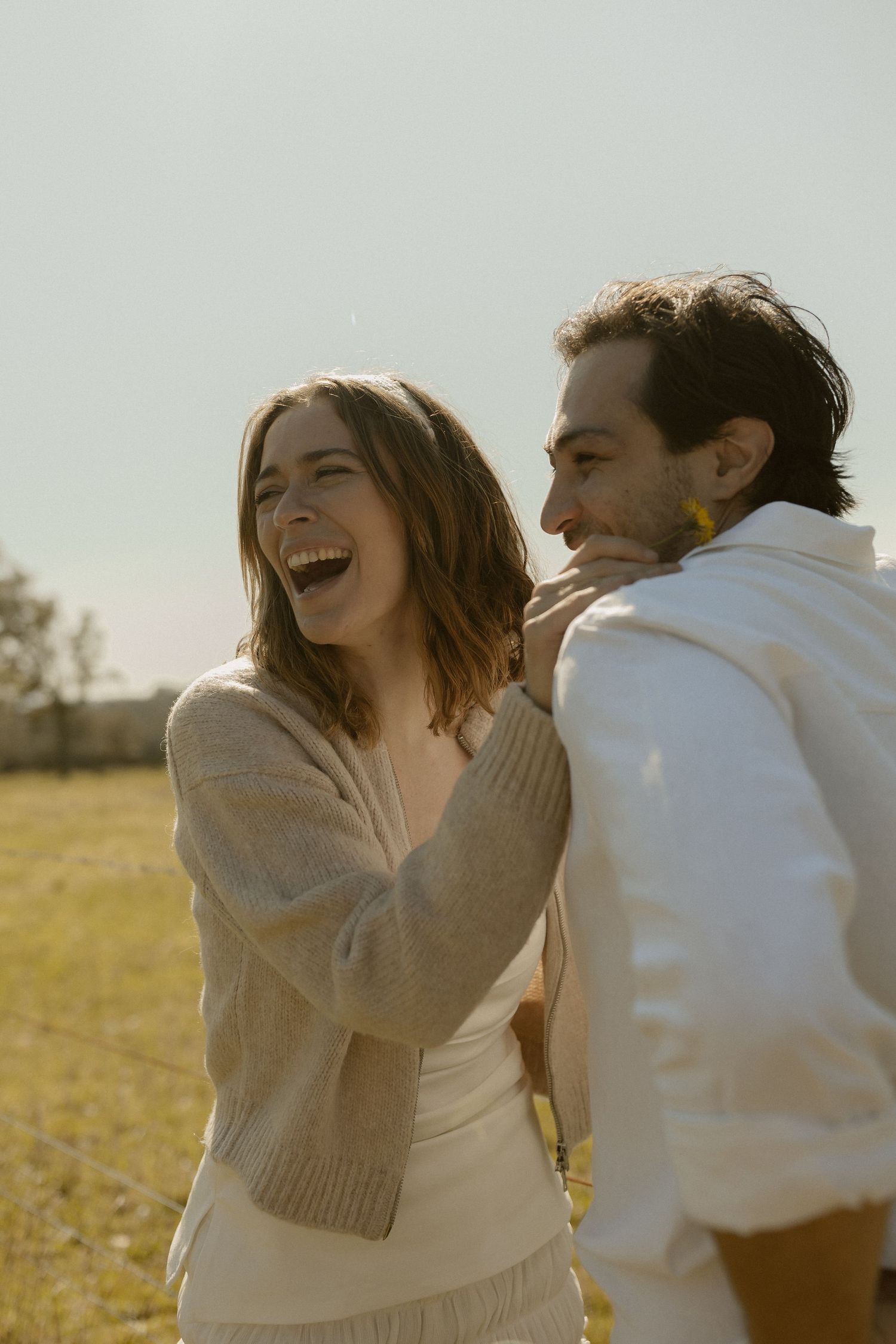 A joyful couple laughs together while embracing in a sun-drenched field.