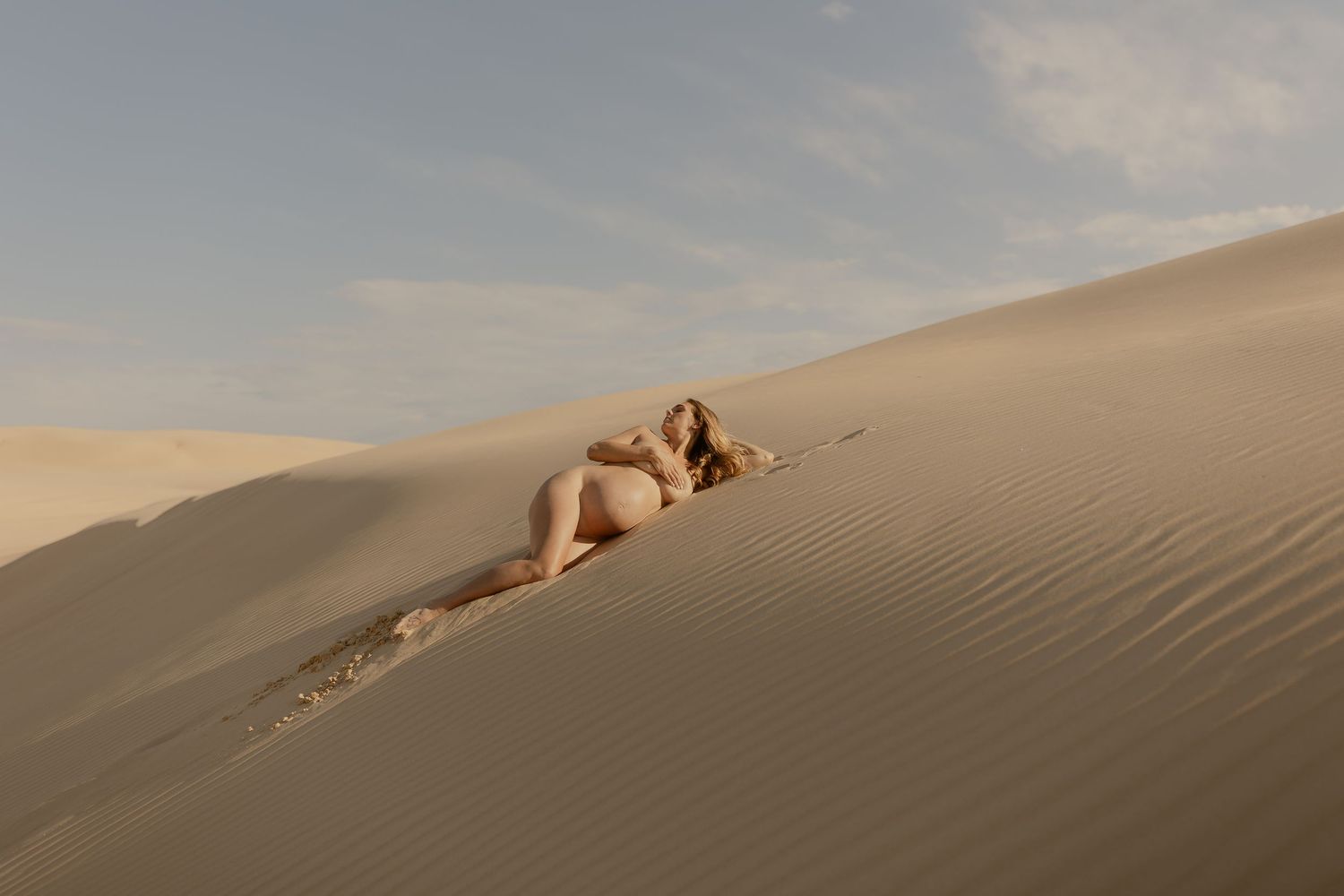 Figure rests gracefully on golden sand dunes at sunset creating a serene desert landscape.