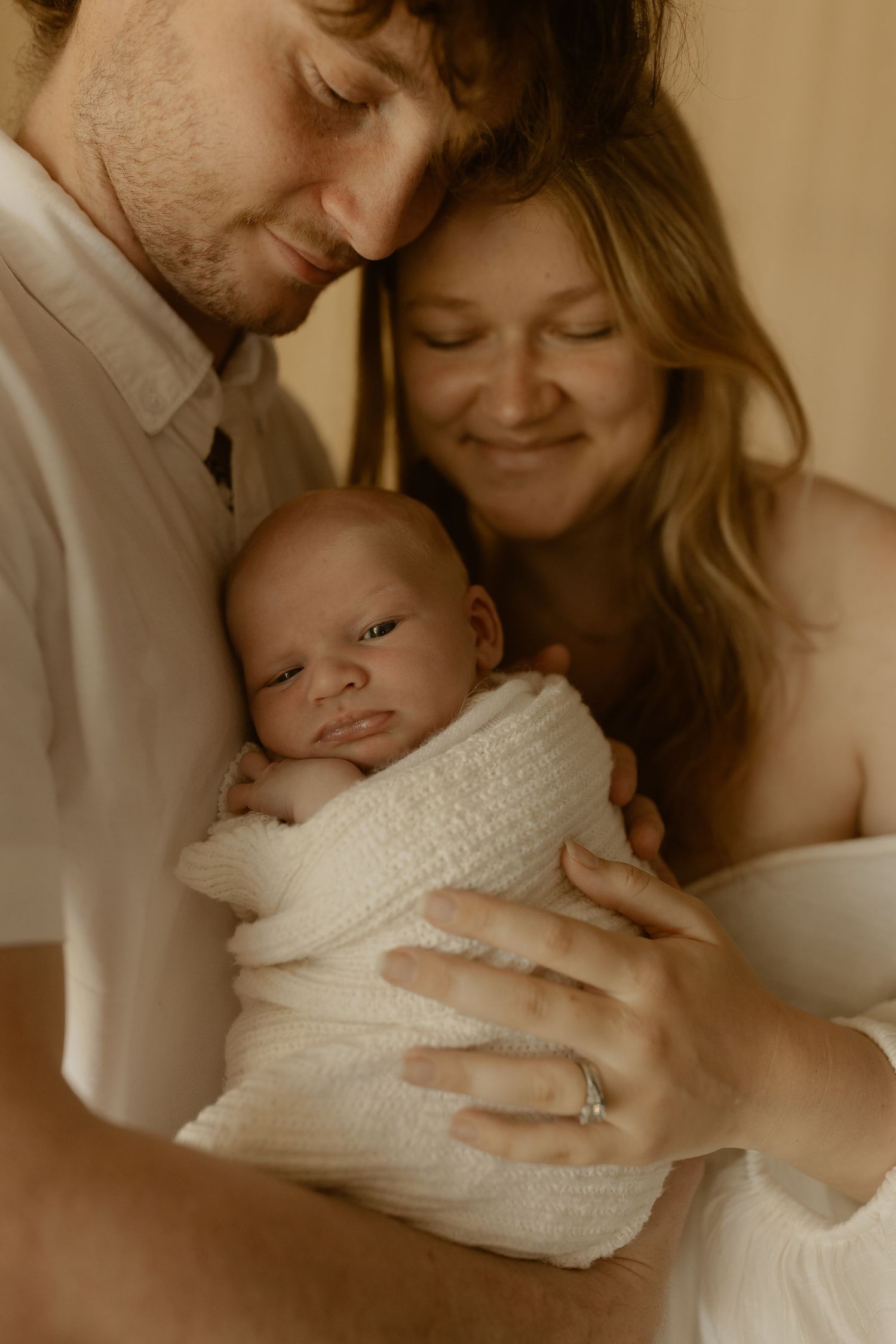 A warm sepia-toned photo sequence showing tender family moments with a newborn baby wrapped in white knit blanket.