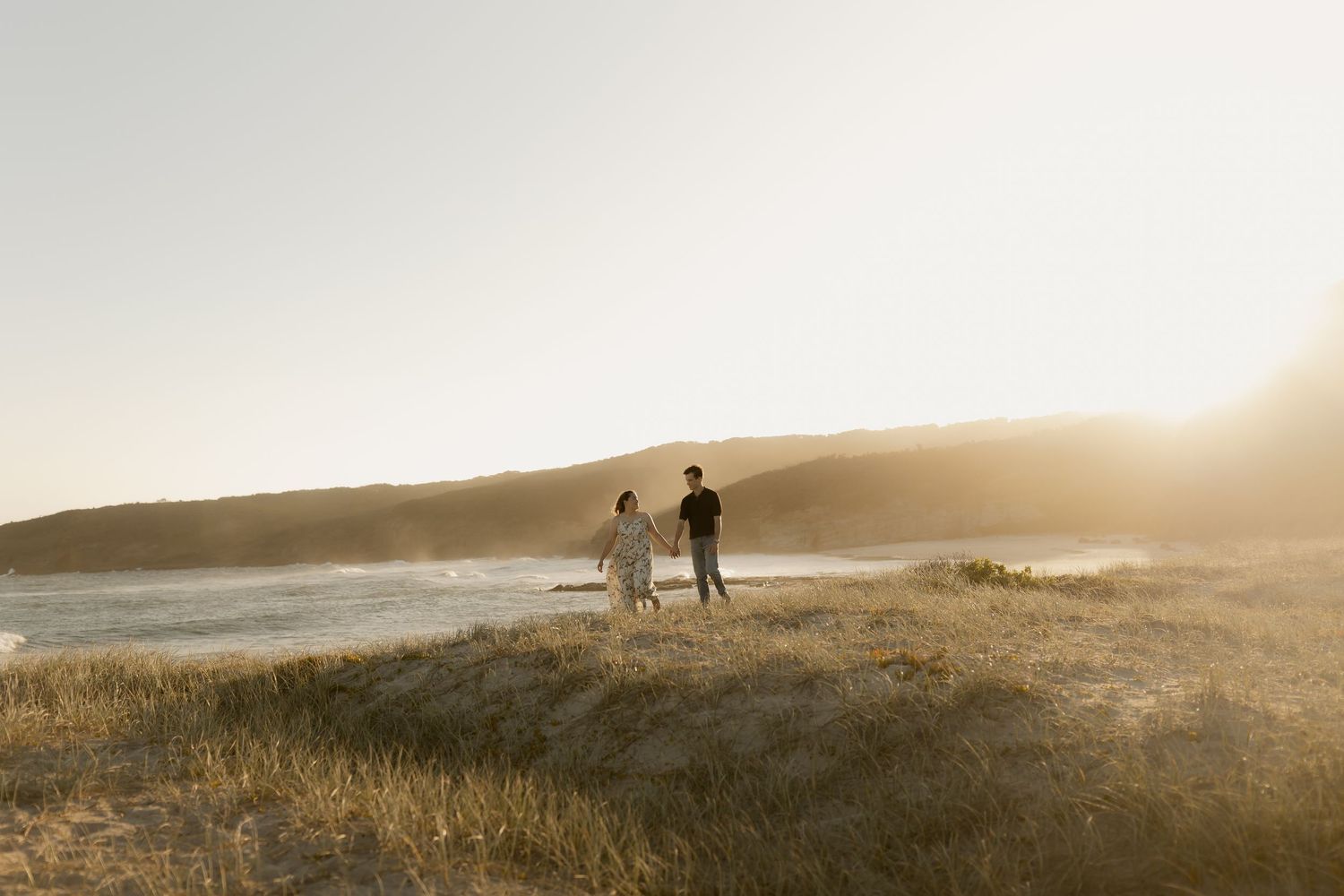 Silhouettes of people walking on a sandy beach at sunset with golden light streaming through misty ocean air.