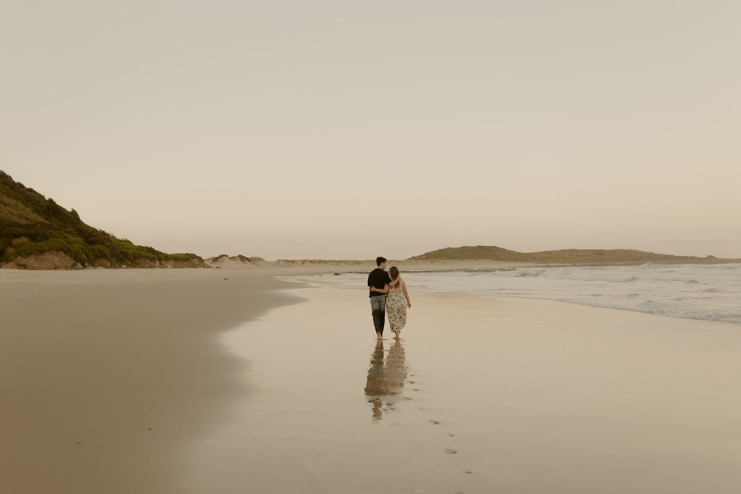 Silhouettes of people walking on a misty beach with distant islands visible on the horizon.
