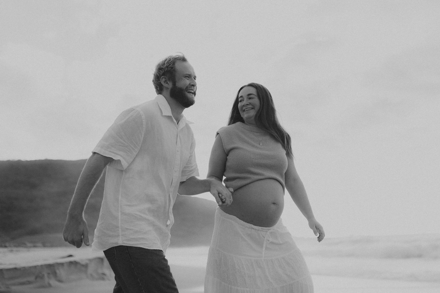 Couple in casual attire walking and smiling together on foggy beach.