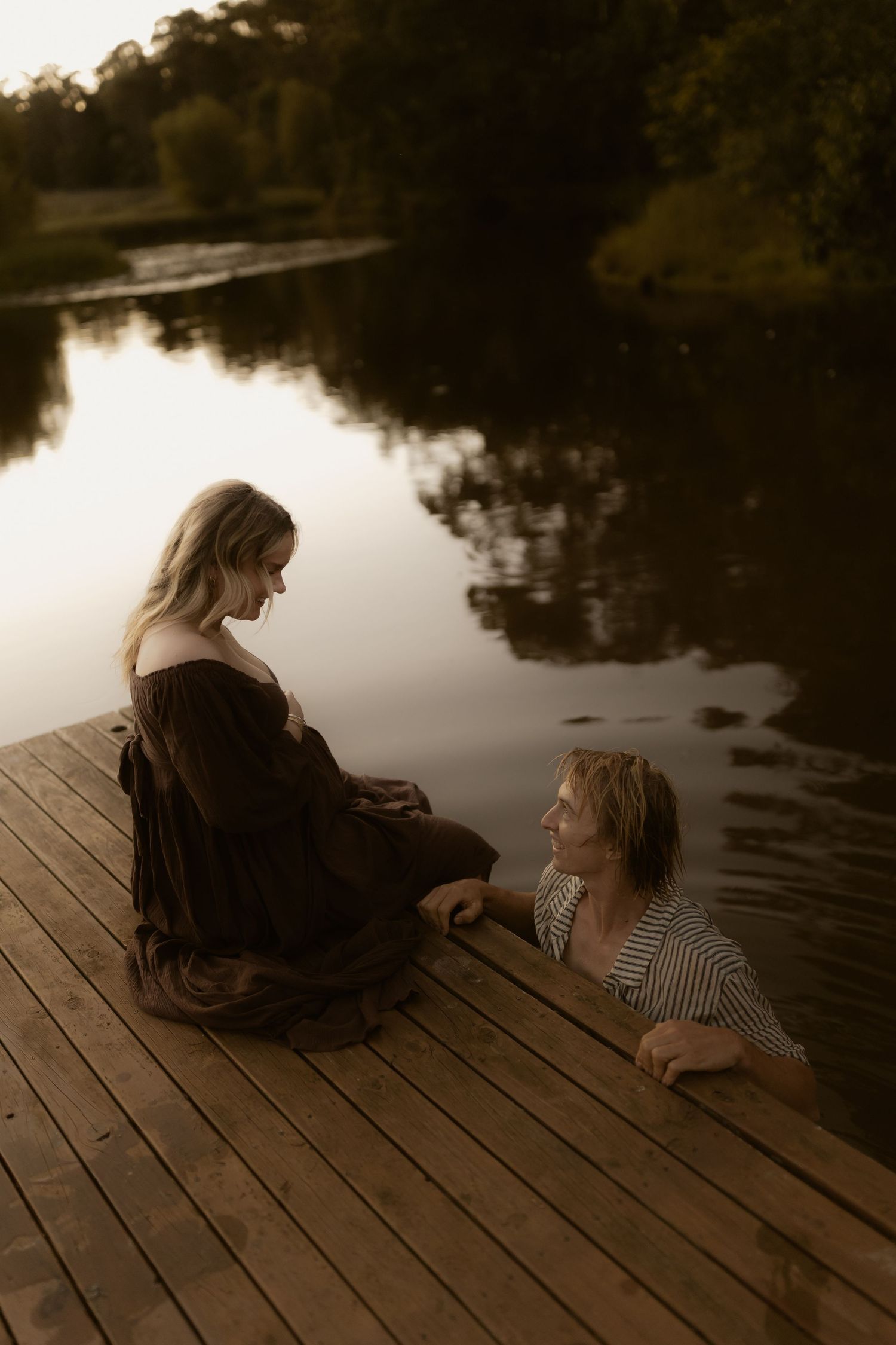 Two figures sitting together on a wooden dock at sunset.