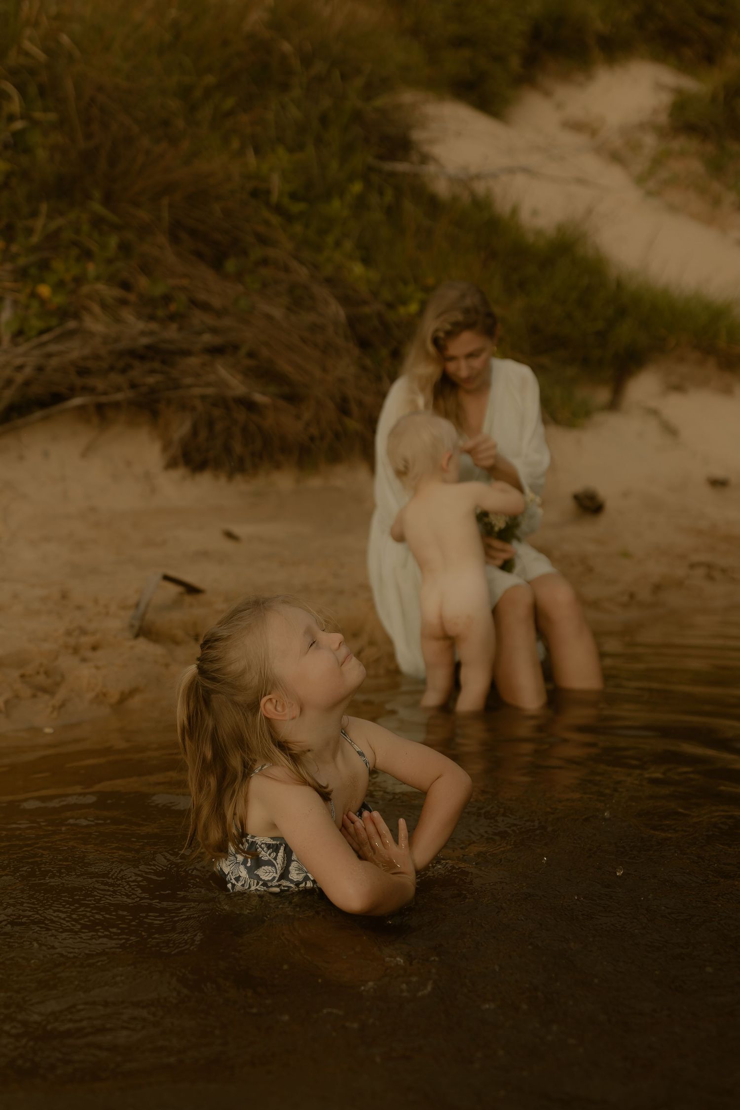 Children splash and play in shallow water at the beach during golden hour.