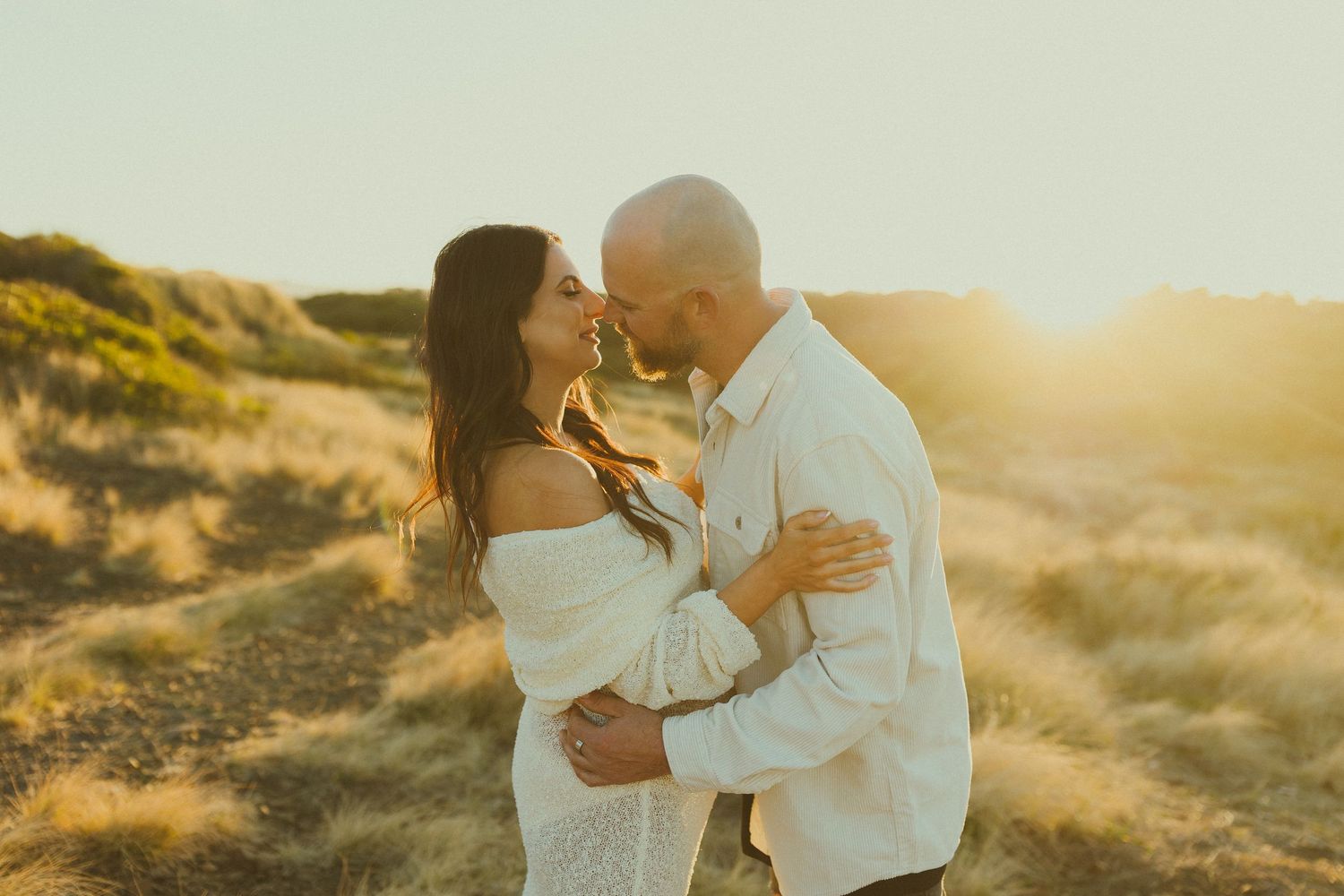 A tender family moment captured in a grassy field at golden hour.
